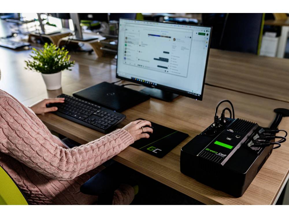 Una persona lavora alla scrivania con un computer, un'applicazione di chat aperta sullo schermo, un'unità tecnologica esterna accanto alla tastiera.