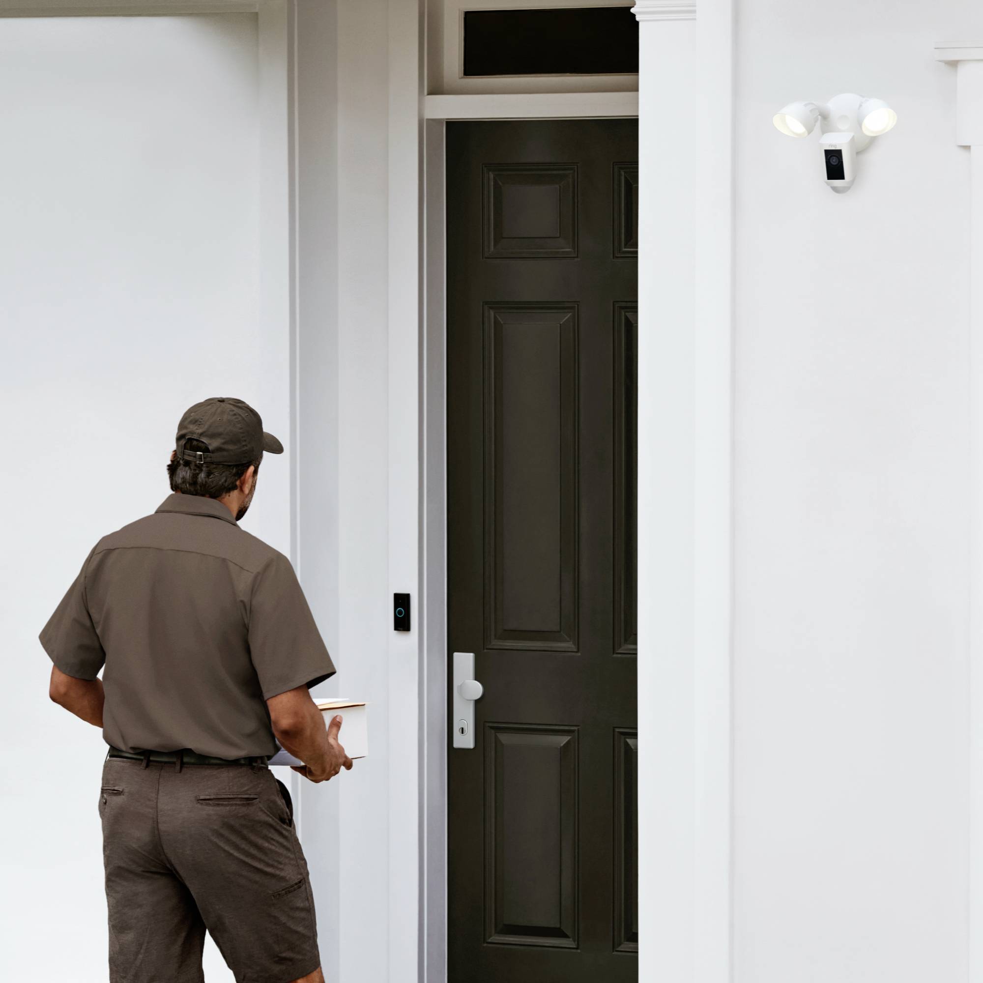 Un corriere è in piedi davanti a una porta d'ingresso con un pacco in mano. Accanto alla porta è installata una telecamera di sicurezza moderna.