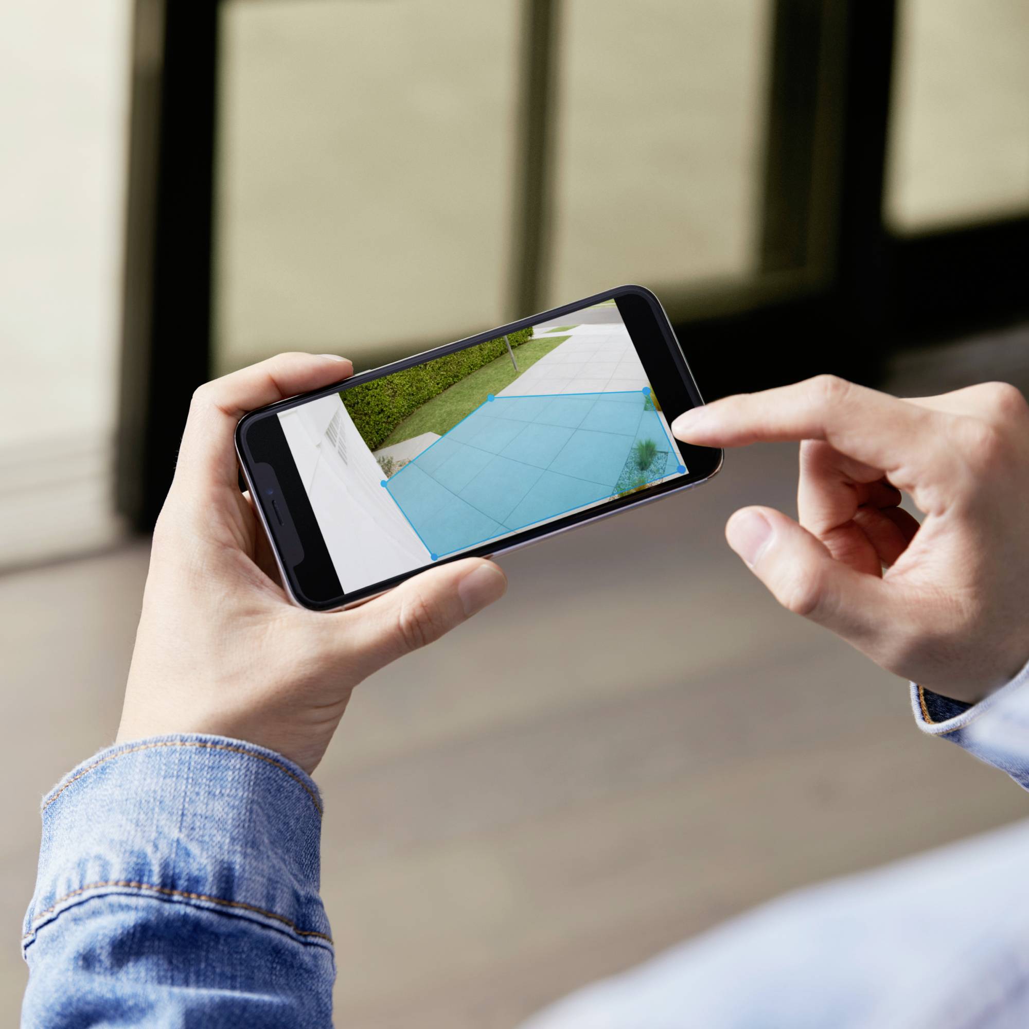 Una mano tiene uno smartphone che mostra la foto di una piscina ad angolo. Sullo sfondo si intravedono delle porte di vetro sfocate.