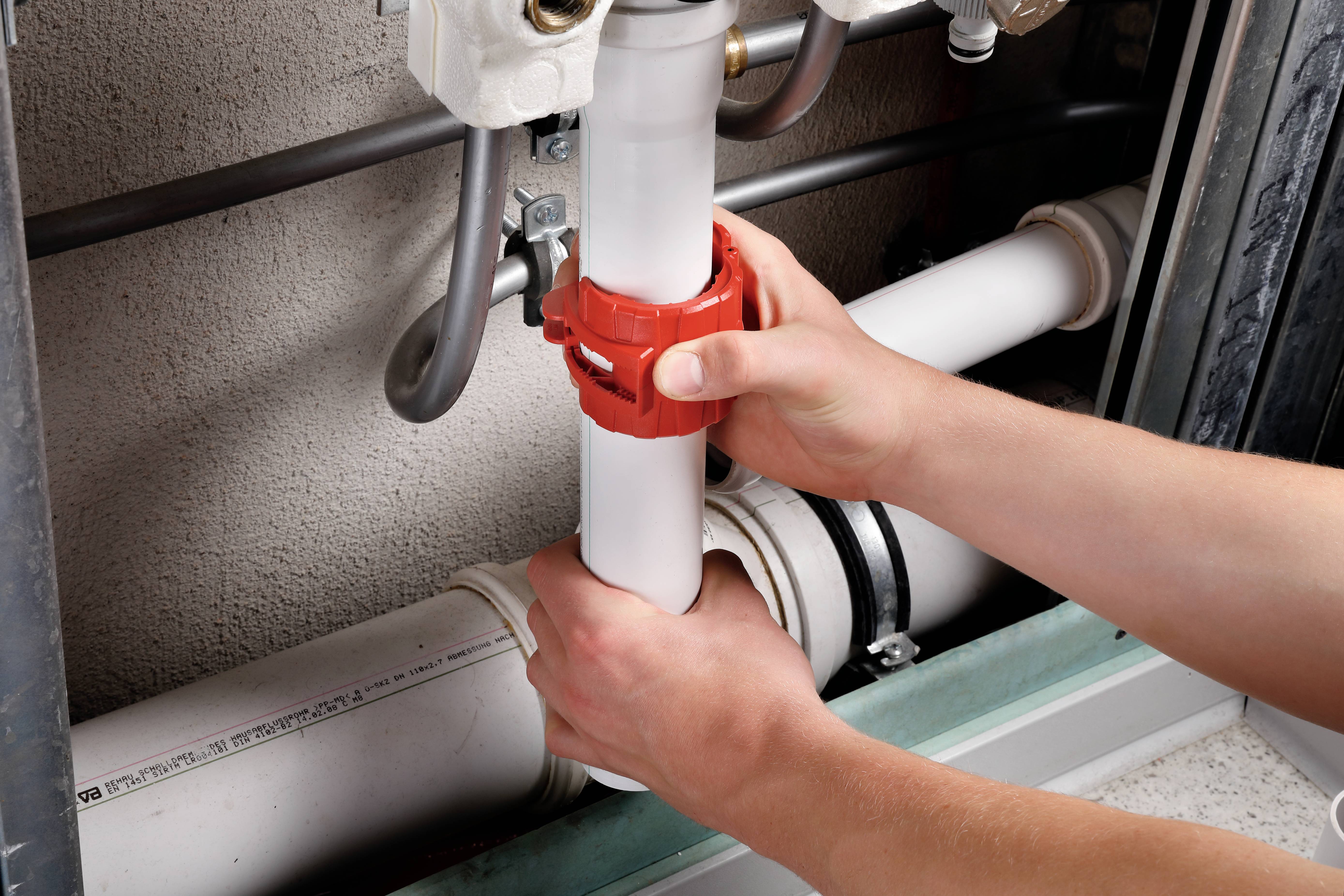 Mani che installano o rimuovono un tubo bianco con un manicotto rosso, probabilmente in un contesto di riscaldamento o impianti idraulici.
