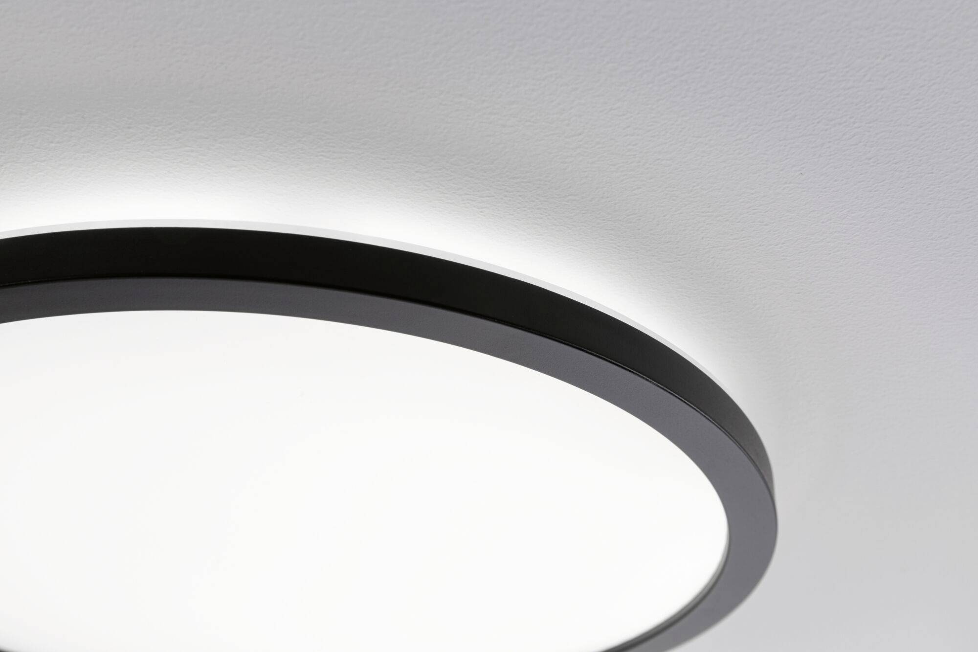 Moderna plafoniera rotonda con cornice nera in una stanza bianca. Emana una luce chiara e uniforme.