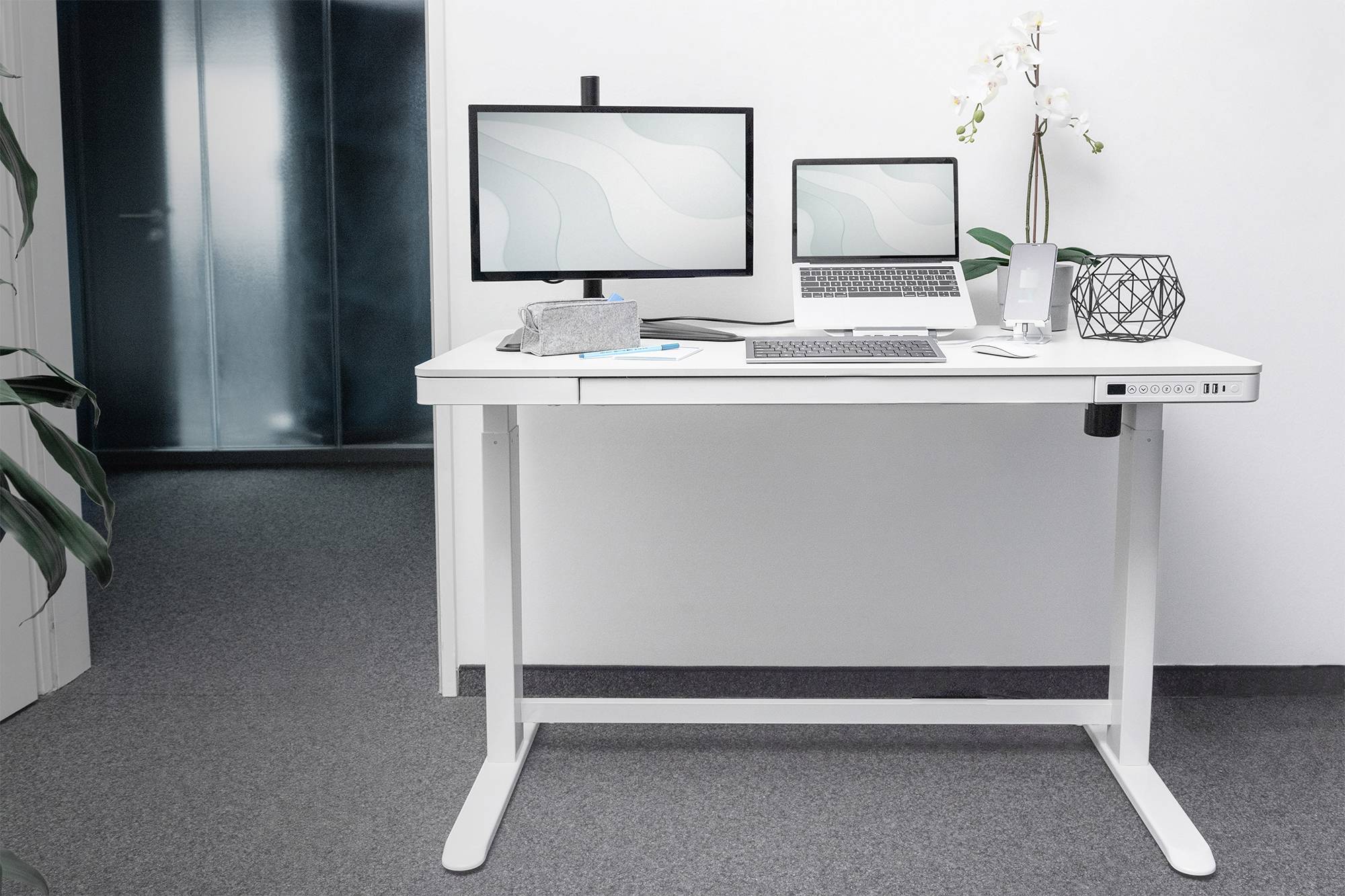 Una scrivania ergonomica moderna con laptop, due monitor, tastiera e decorazioni come una pianta in un ufficio.