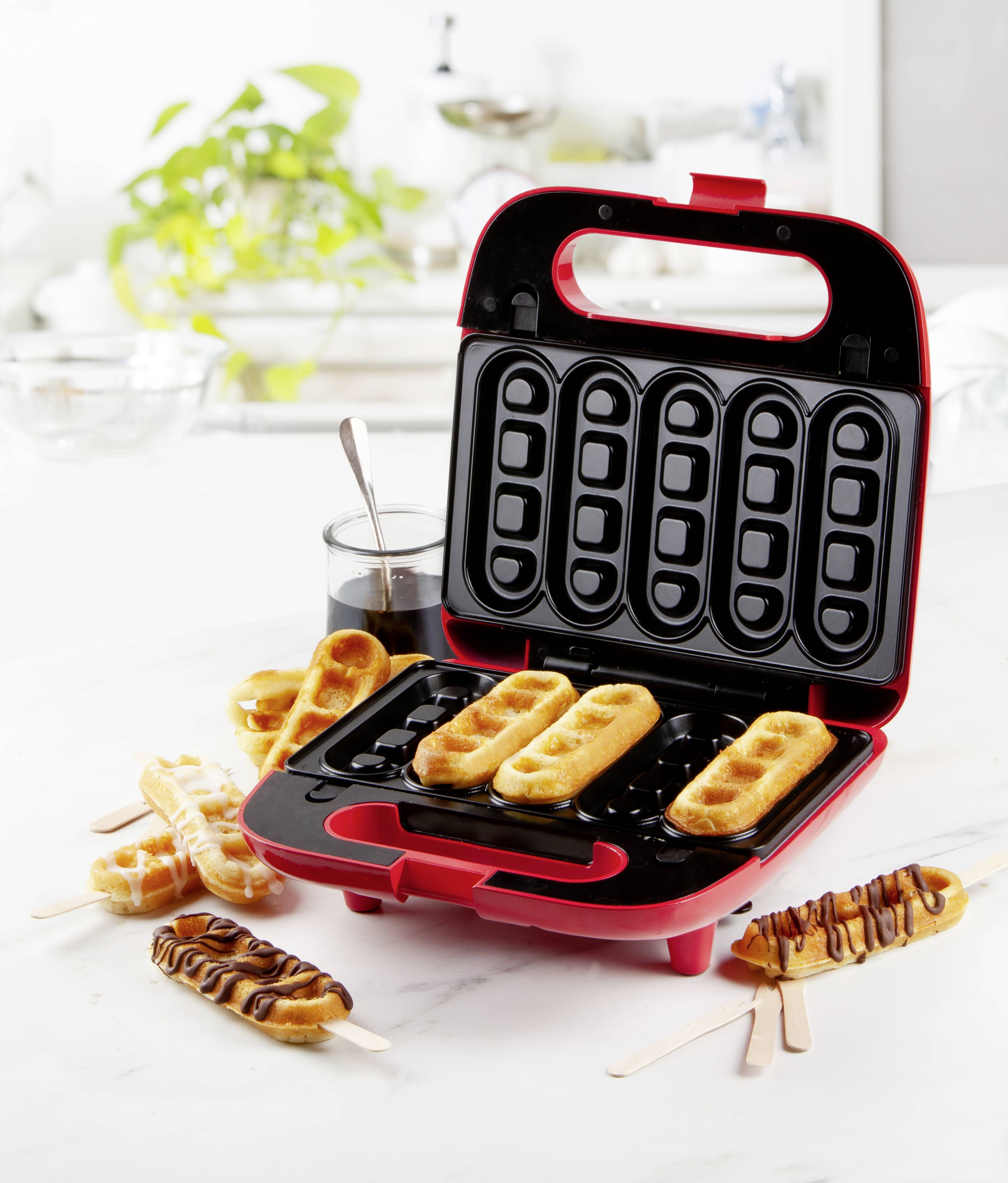 Macchine per waffle in una cucina con diversi waffle su stecchi, alcuni decorati con glassa al cioccolato.