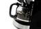 Macchina da caffè con caraffa di vetro riempita a metà, base nera e indicatore del livello del caffè visibile, su sfondo bianco.