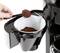 Una mano versa il caffè macinato con un cucchiaio dosatore nel filtro di una macchina da caffè.