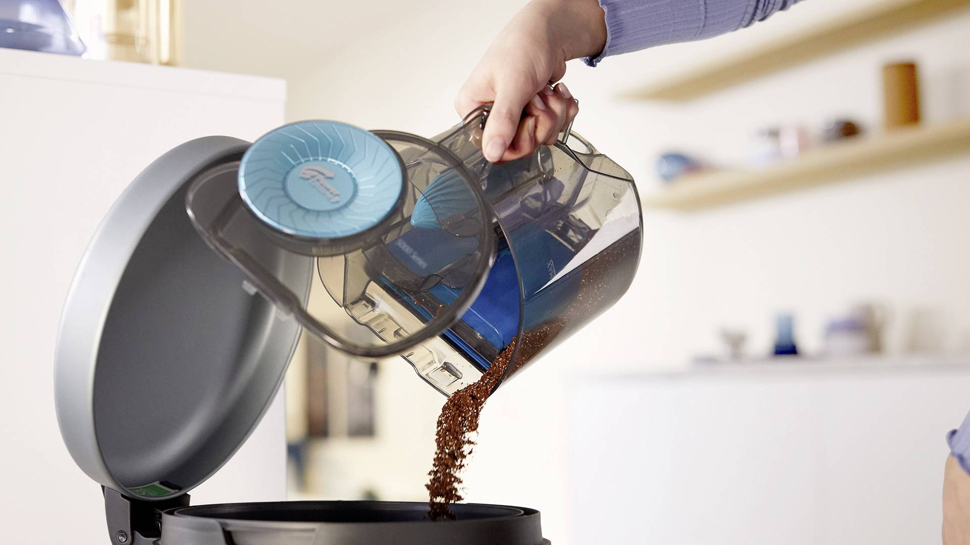 Una persona svuota il contenitore della polvere di un aspirapolvere senza sacchetto in un cestino dei rifiuti.