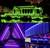 Un padiglione illuminato nel parco si riflette nell'acqua, in un verde vivace, accompagnato da strutture moderne con luce viola e blu.