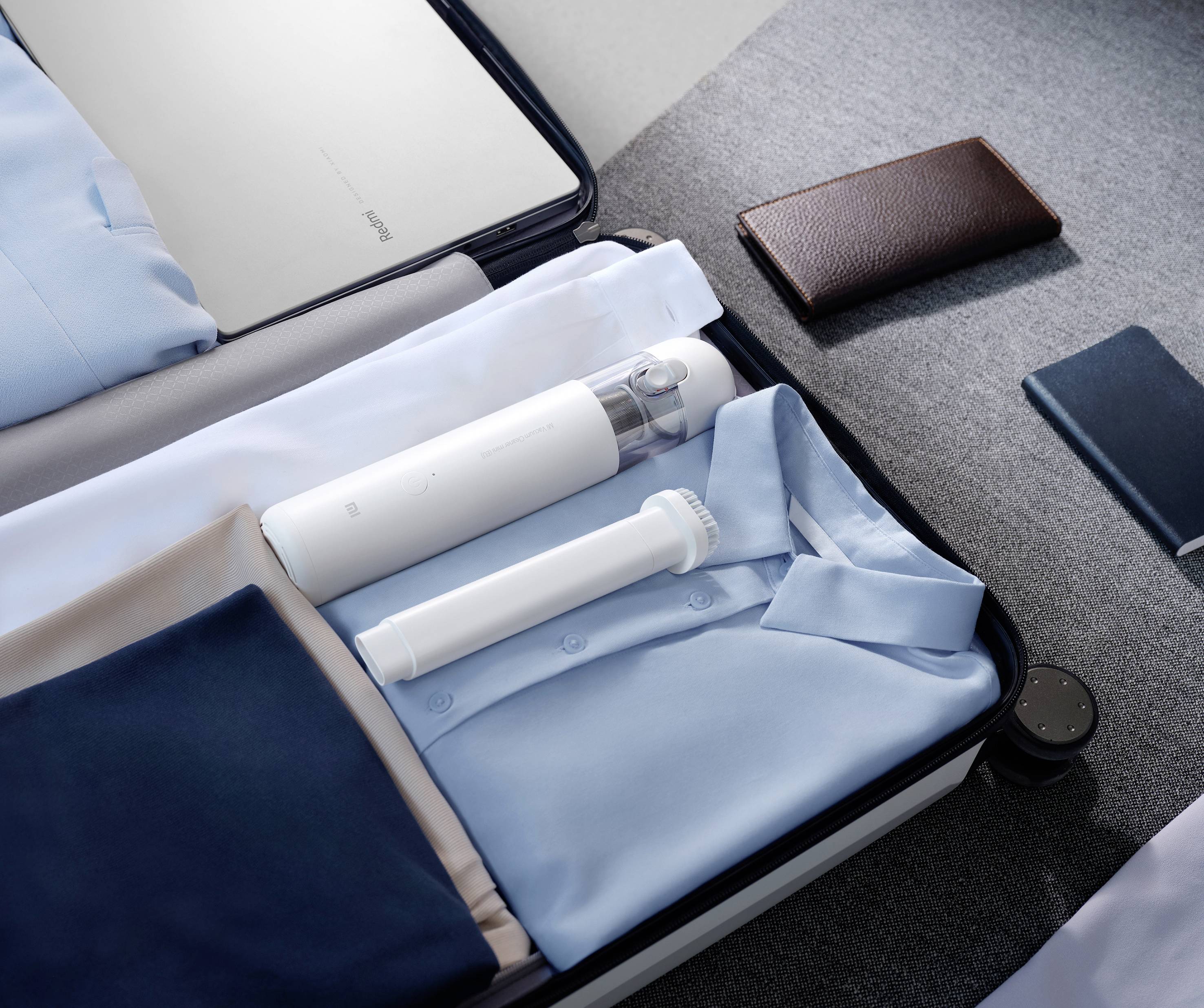 Una valigia aperta su un letto mostra camicie blu accuratamente piegate e una bottiglia da viaggio bianca. Accanto si trova un portafoglio marrone.