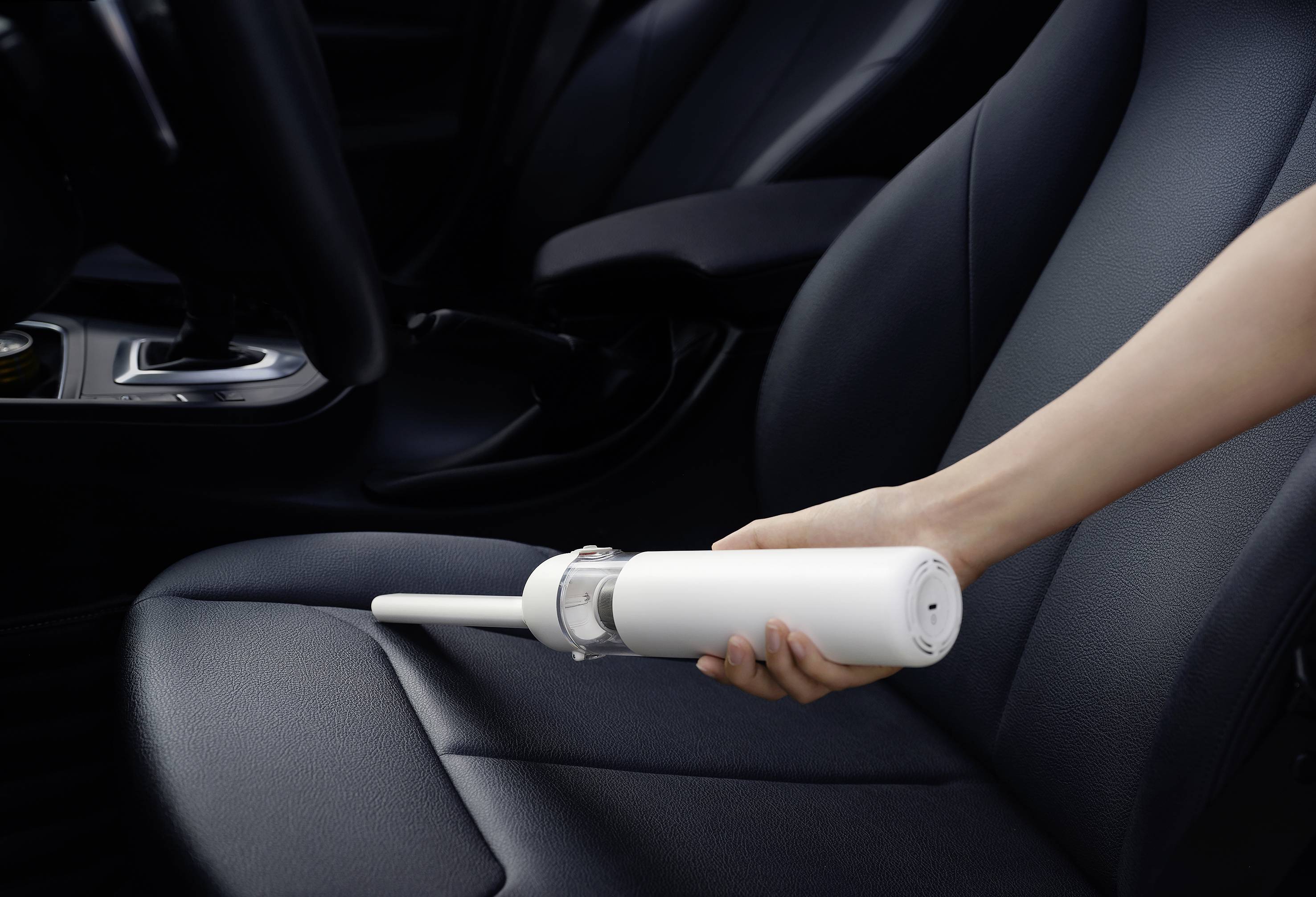 Una persona sta pulendo il sedile dell'auto con un aspirapolvere bianco portatile all'interno di un veicolo.