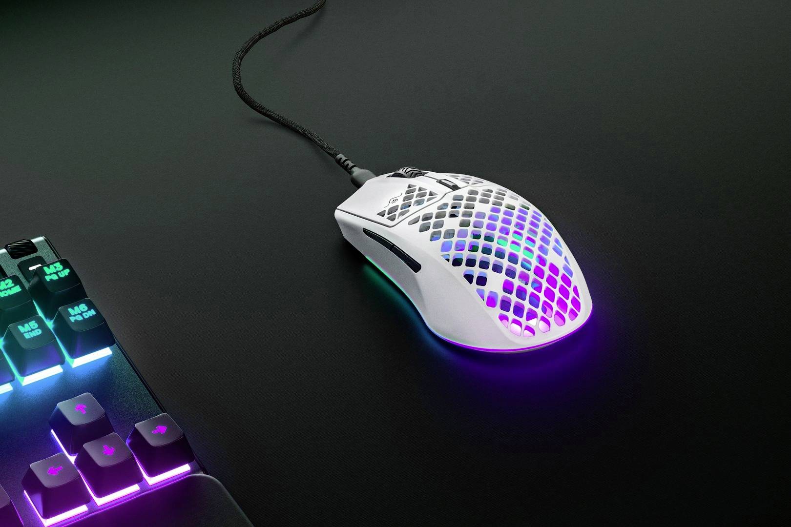 Mouse da gaming bianca con illuminazione RGB su un tavolo nero accanto a una tastiera illuminata.