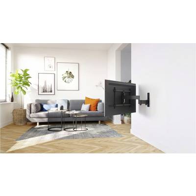Un soggiorno con un divano, cuscini e un supporto TV a parete. Piante e arte parietale creano un'atmosfera accogliente.