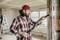 Uomo con camicia a quadri e cappello rosso che pulisce una trave in legno con un aspirapolvere in una stanza in ristrutturazione.