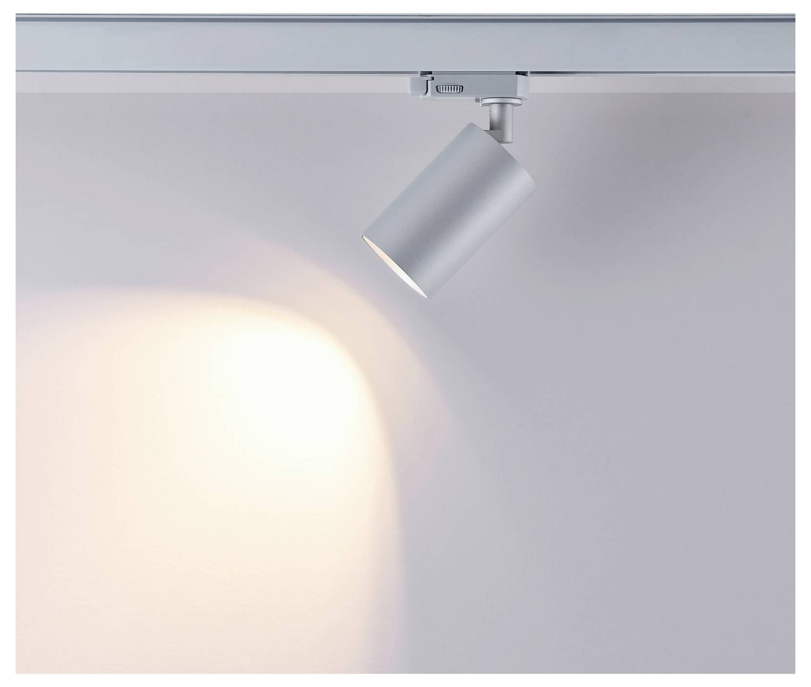 Un singolo binario di illuminazione argentato proietta un caldo punto di luce su una parete grigio chiaro e spoglia.