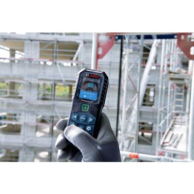 Una persona sta utilizzando un misuratore laser di distanza Bosch per effettuare misurazioni precise in un edificio di costruzione in acciaio non completato.