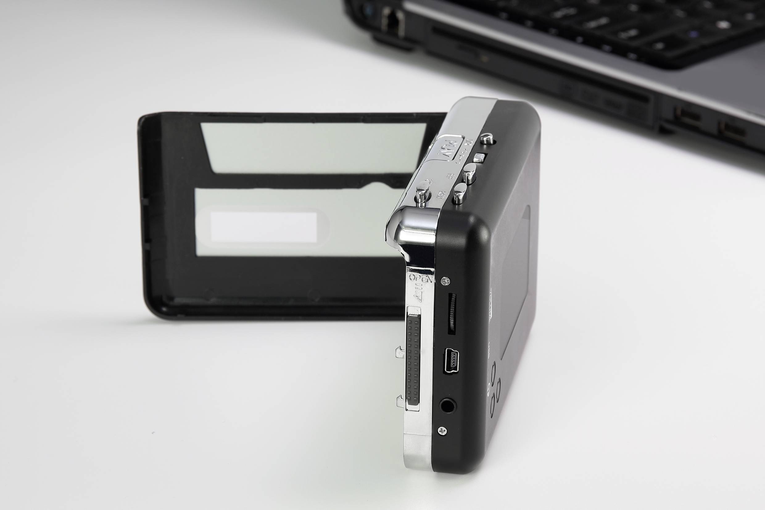 Fotocamera digitale con display pieghevole, su un tavolo bianco accanto a una tastiera di laptop aperta.