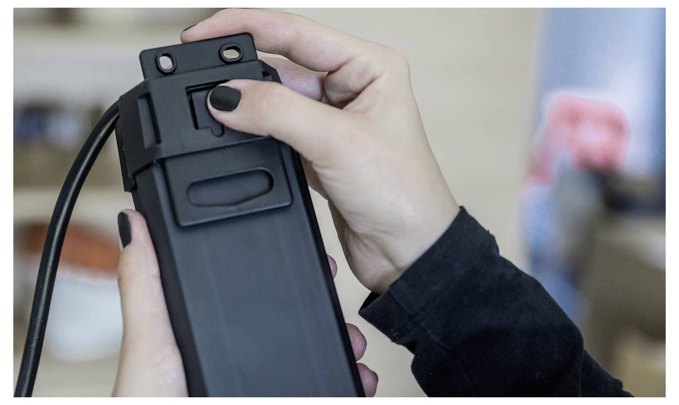 Primo piano delle mani che fissano una custodia per smartphone nera con un cavo o un laccio al dispositivo, con uno sfondo interno sfocato.