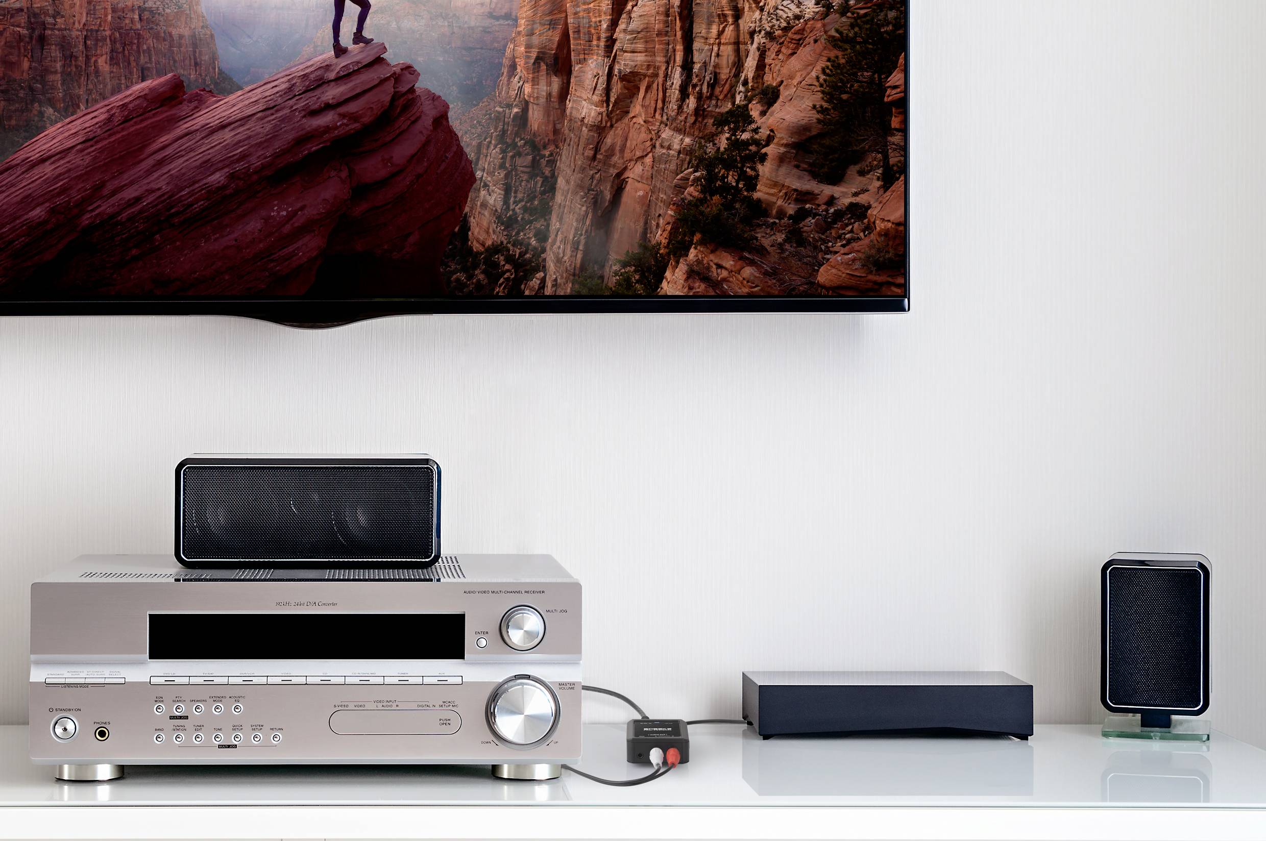 Configurazione home cinema con amplificatore, altoparlanti e TV che mostra un paesaggio.