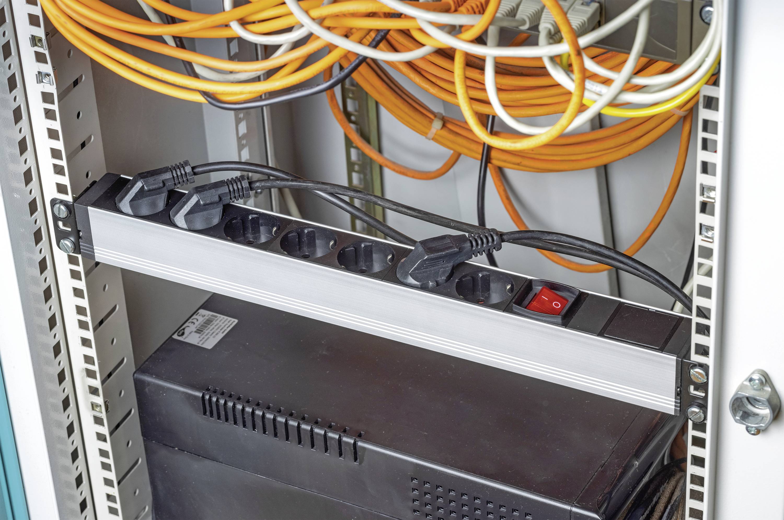 Un armadio server aperto con una multipresa, diversi cavi collegati e un dispositivo sottostante.