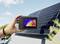 Una mano tiene una termocamera sopra un pannello solare; il display mostra un'immagine termica del pannello per verificare la distribuzione della temperatura.