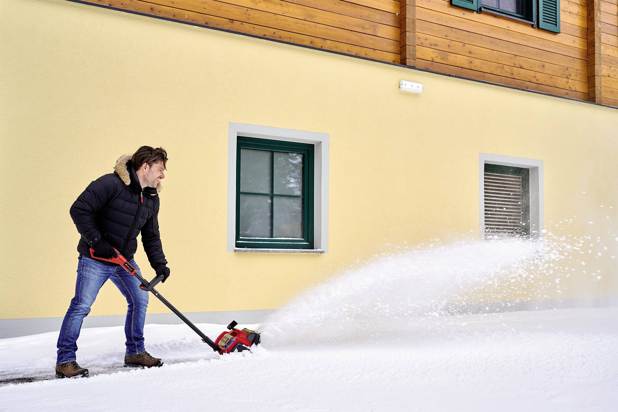 Un uomo rimuove la neve davanti a una casa utilizzando una turbina per la neve. Indossa abiti caldi e lavora su un terreno coperto di neve.