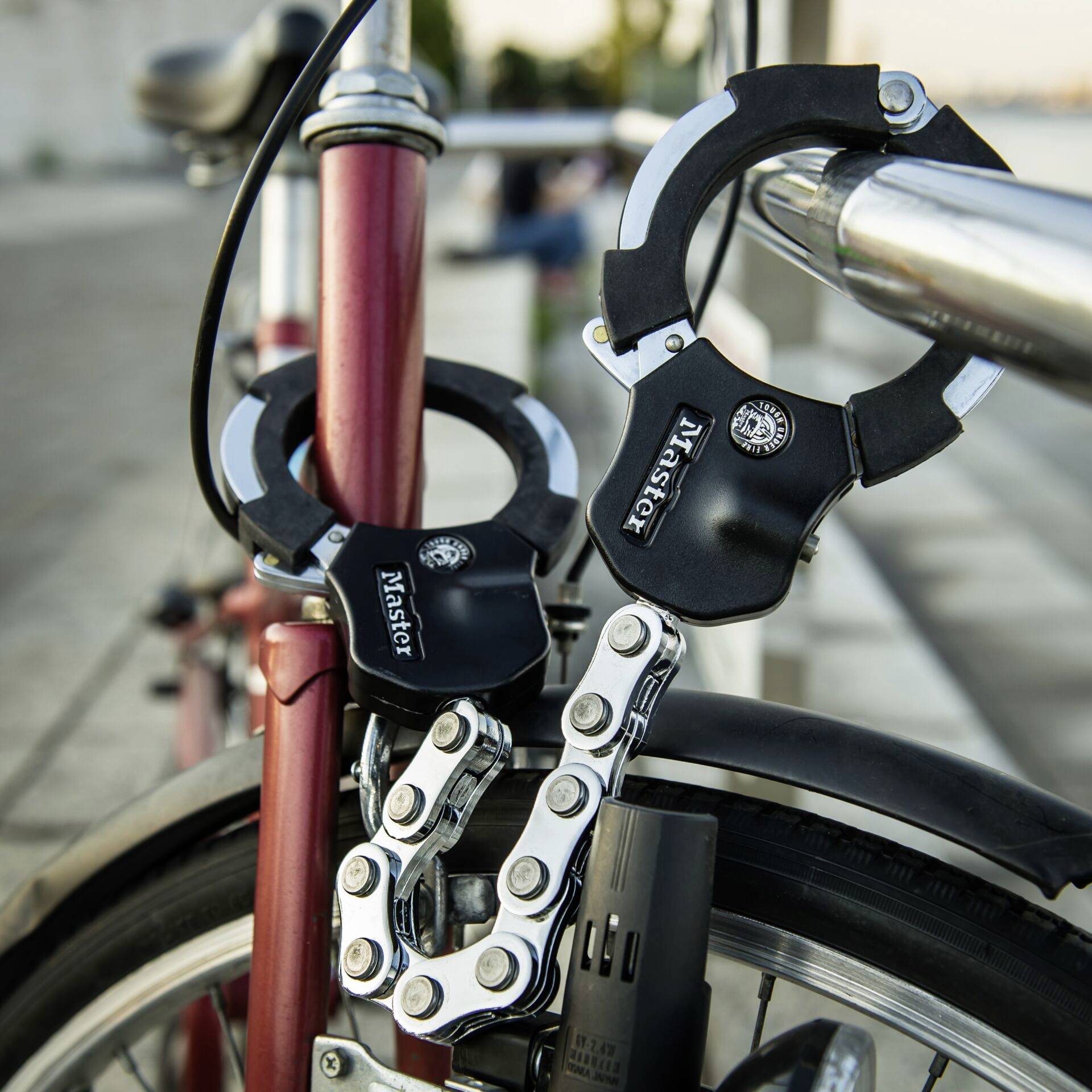 Una bicicletta rossa è fissata con un robusto lucchetto a U a un corrimano metallico. Persone sfocate sullo sfondo.