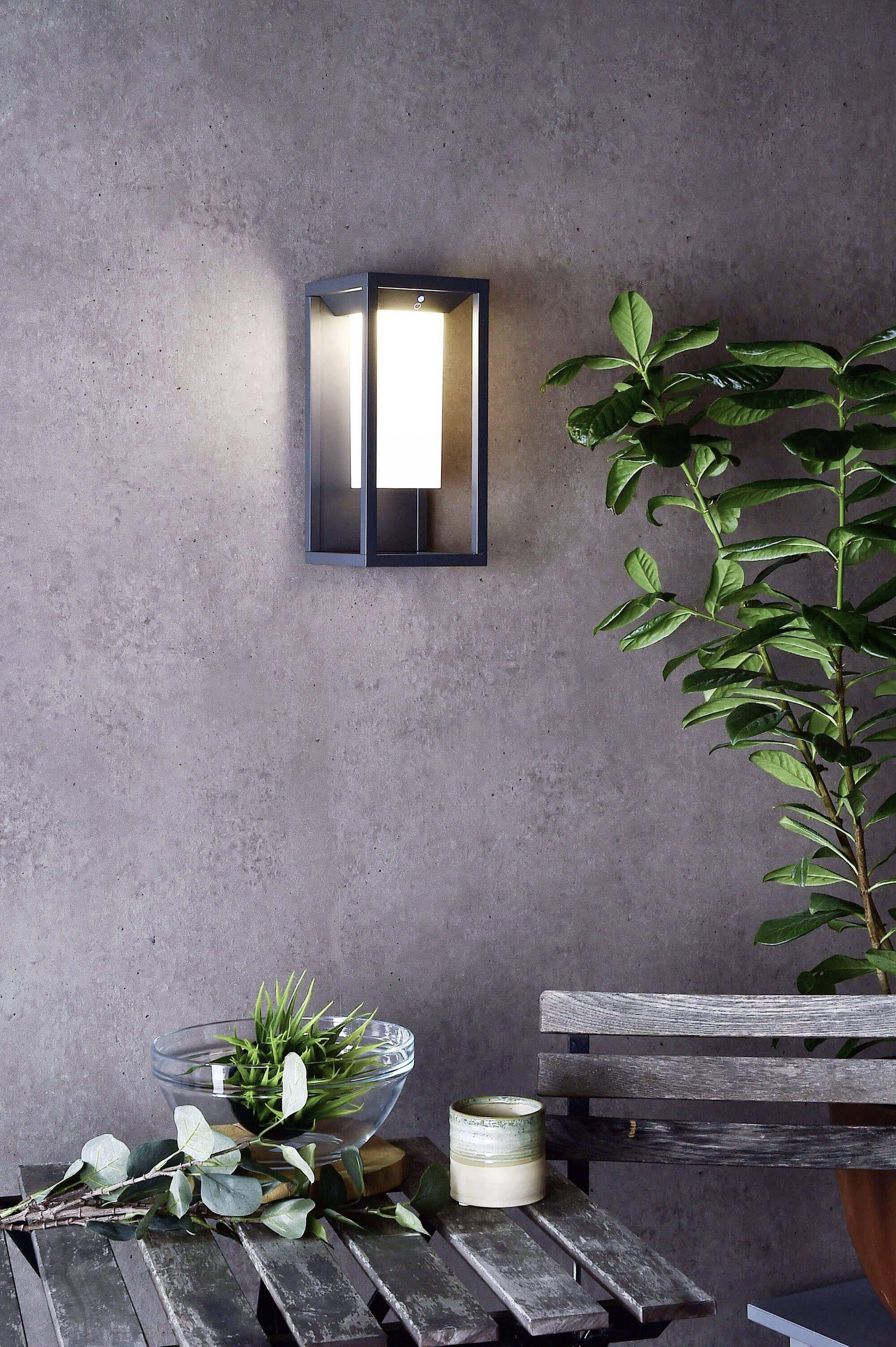 Applique da parete illumina dolcemente accanto a un tavolo con una pianta e una candela in uno spazio moderno e minimale.