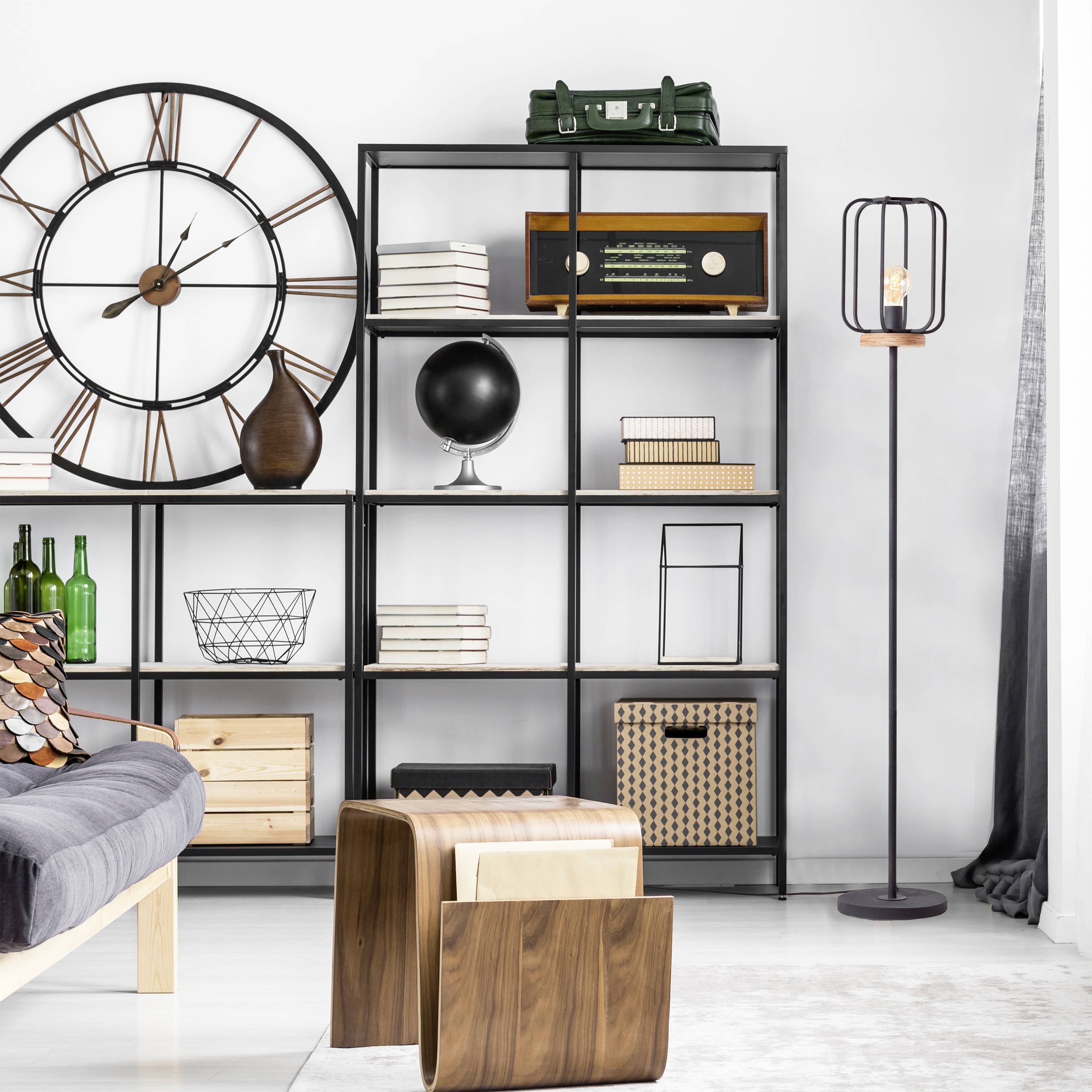 Soggiorno con divano grigio, grande orologio da parete, scaffali neri pieni di libri e decorazioni, e tavolini in legno. Design elegante e moderno.