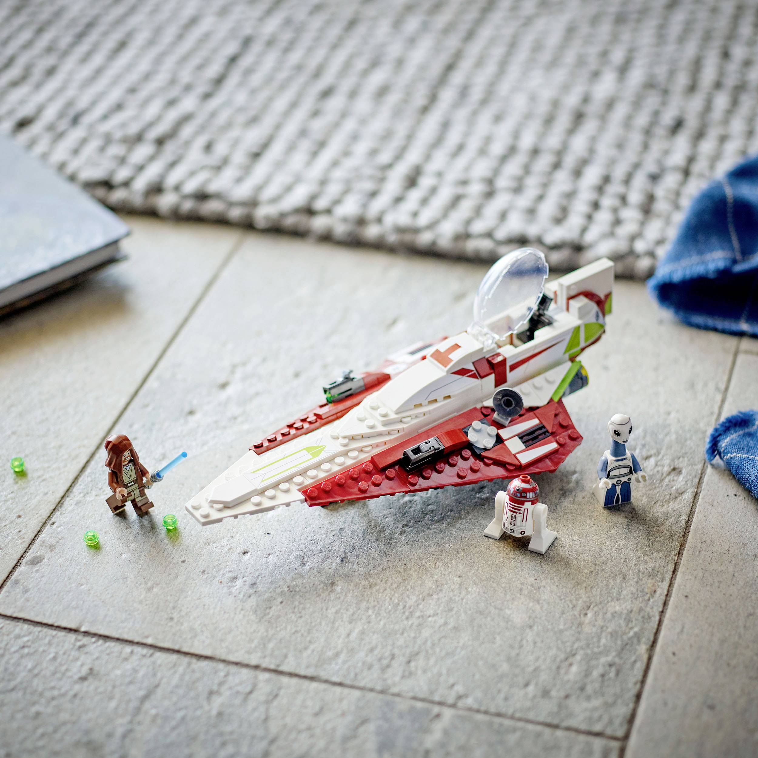 Una nave spaziale costruita con mattoncini che mostra tre figure: un Jedi con la spada laser, un droide e un guerriero su un pavimento.