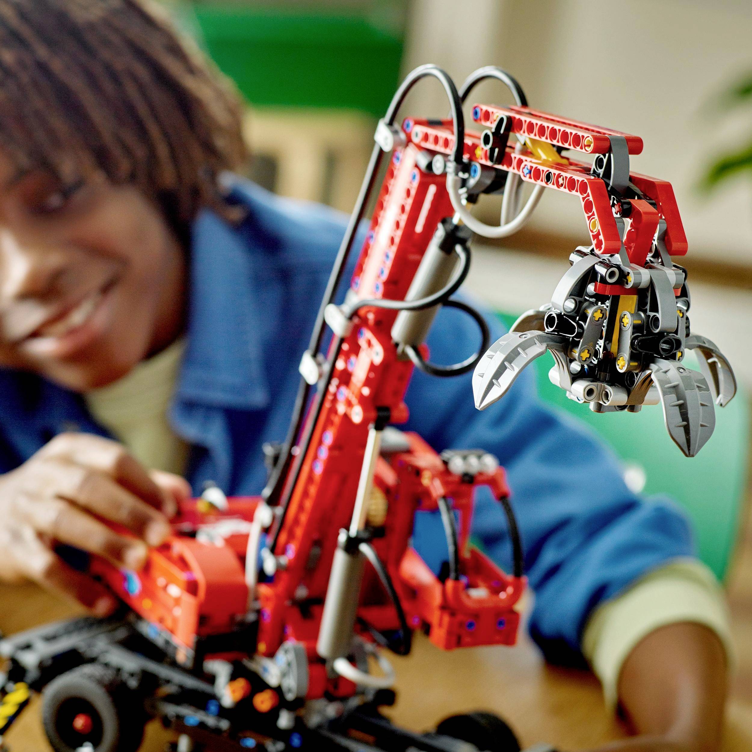 Una persona sta azionando un braccio robotico LEGO rosso poggiato su un tavolo. L'attenzione è concentrata sul braccio, che mostra meccanismi complessi.