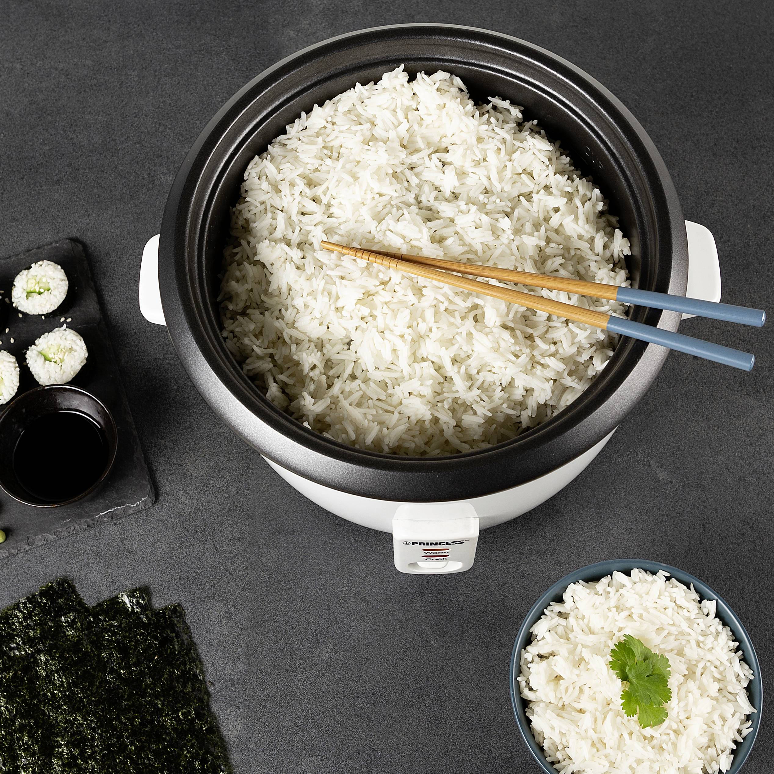 Pentola per riso con riso appena cotto e bacchette, circondato da ingredienti per sushi e una ciotolina di riso con coriandolo.