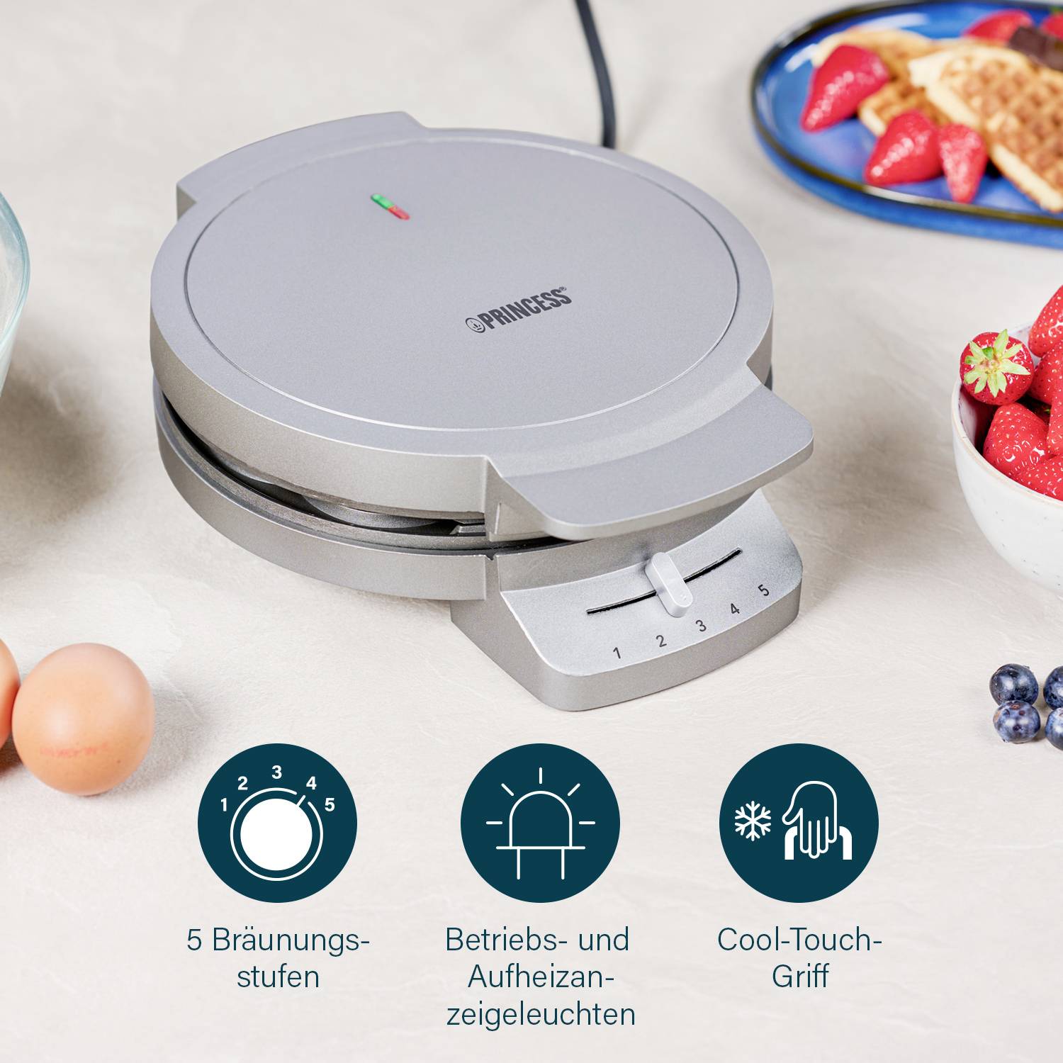 'Piastra per waffle con 5 livelli di doratura, spie di funzionamento e riscaldamento e impugnatura Cool-Touch, circondato da uova e frutta.'