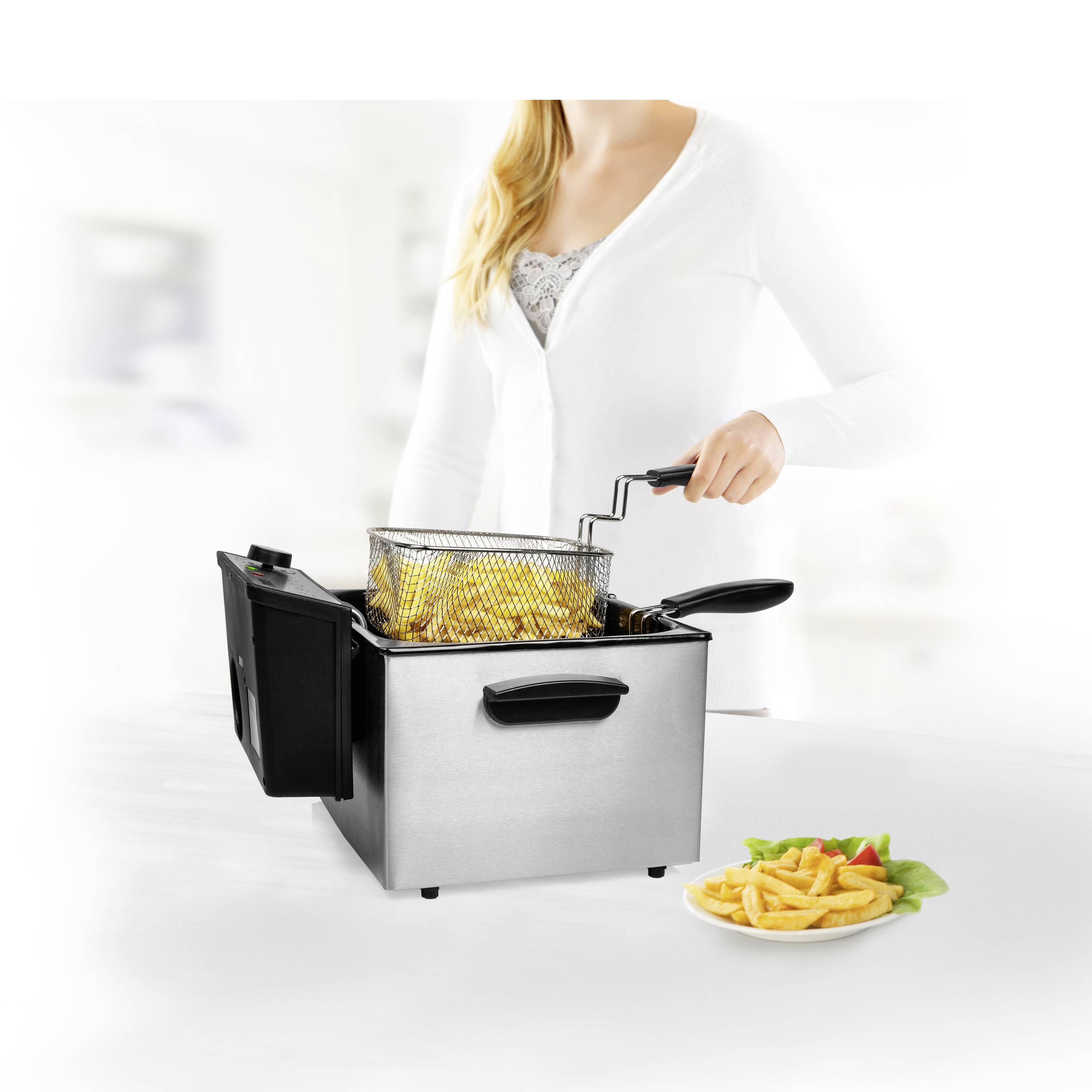 Una persona sta utilizzando una friggitrice per preparare patatine fritte. Un piatto con patatine fritte è posizionato accanto su un tavolo.