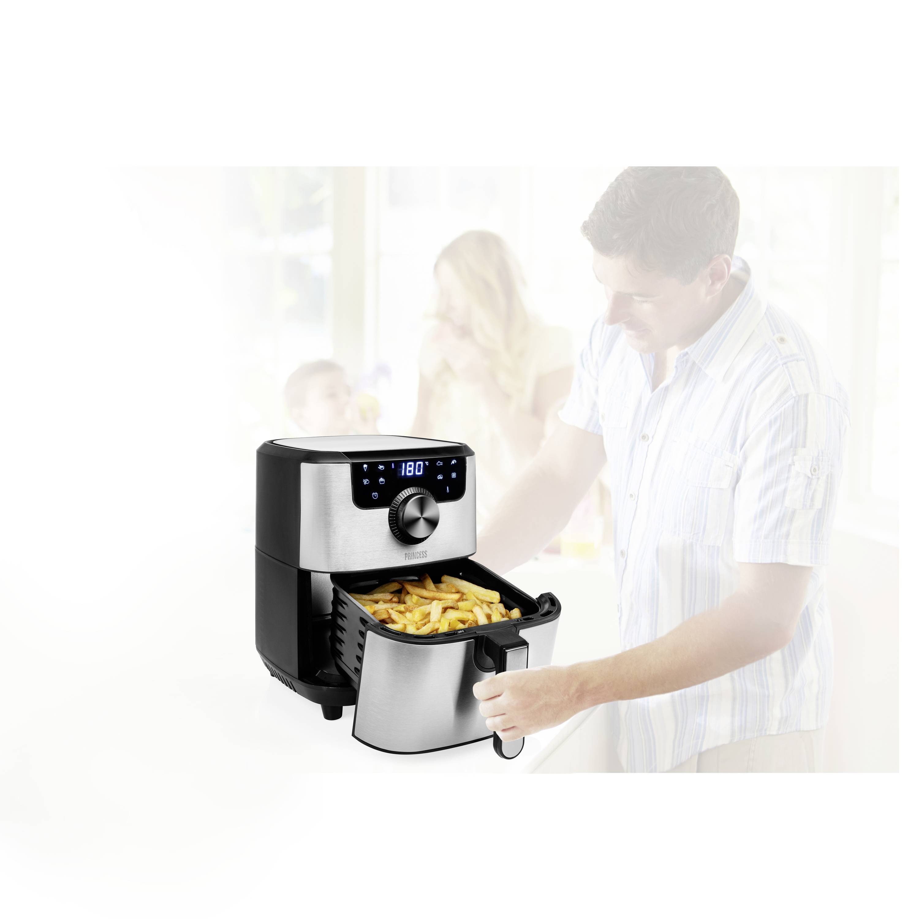 Una friggitrice ad aria calda con display digitale sta friggendo patatine fritte. Sullo sfondo, sfocata, si intravede una famiglia con due bambini.