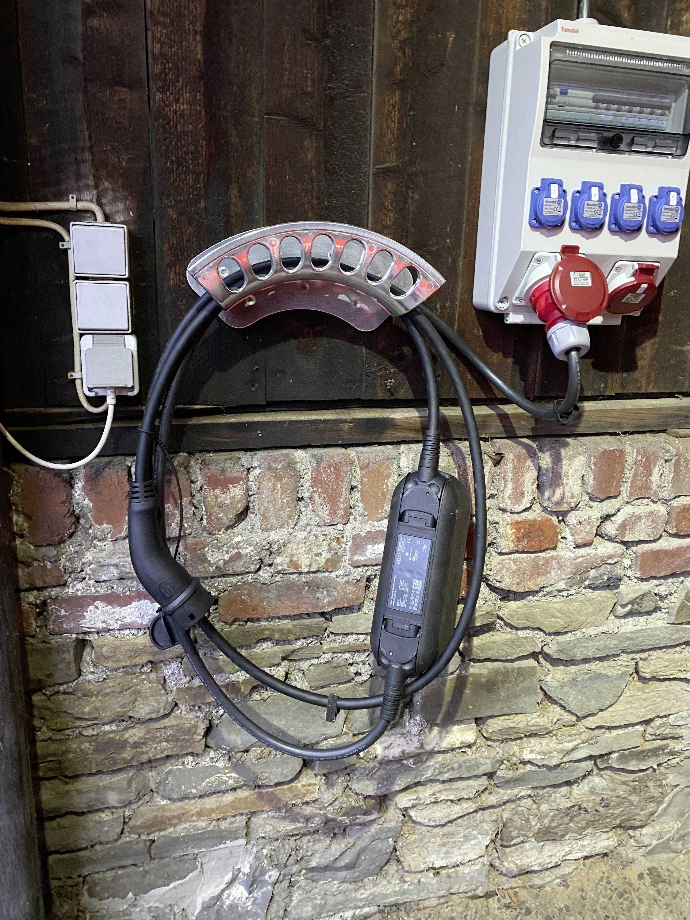 Stazione di ricarica per veicoli elettrici su un muro di mattoni; cavi e connettori visibili; pronta all'uso.
