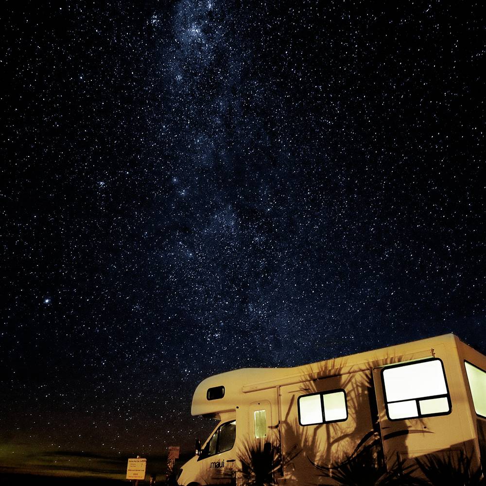 Un camper è parcheggiato sotto un cielo notturno limpido e pieno di stelle, in basso a destra nell'immagine.