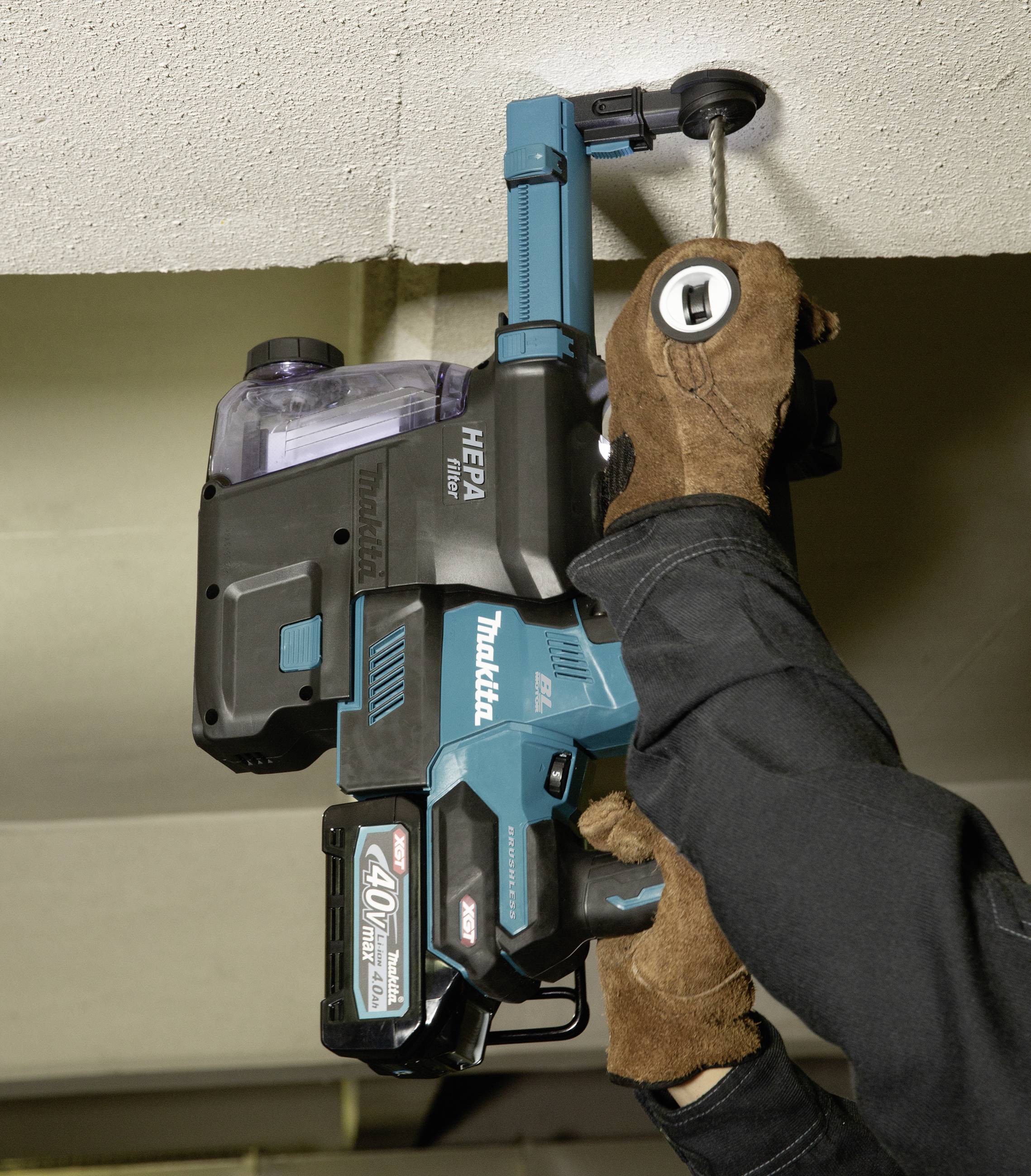 Un lavoratore utilizza un trapano elettrico blu per forare un soffitto. Indossa guanti marroni per la protezione.