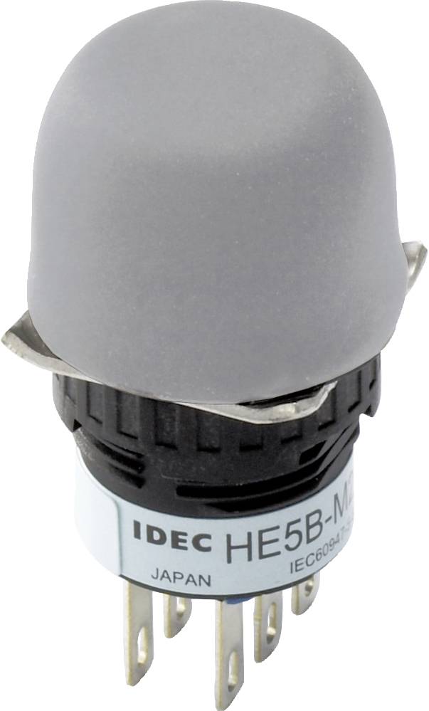 Un pulsante grigio di IDEC con marcatura 'HE5B-M', adatto per quadri elettrici. Sei contatti metallici nella parte inferiore.