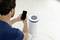 Un uomo controlla un purificatore d'aria posto sul pavimento utilizzando il proprio smartphone. Il display mostra informazioni sulla qualità dell'aria.