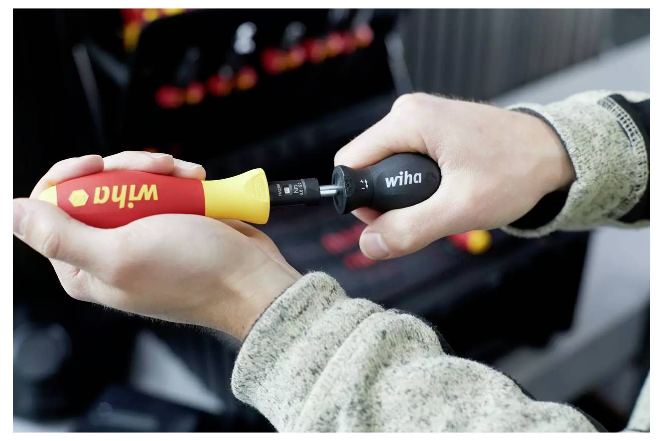 Due mani tengono un cacciavite multi-bit. Una mano afferra il manico etichettato "Wiha" e l'altra tiene una punta intercambiabile in un supporto.