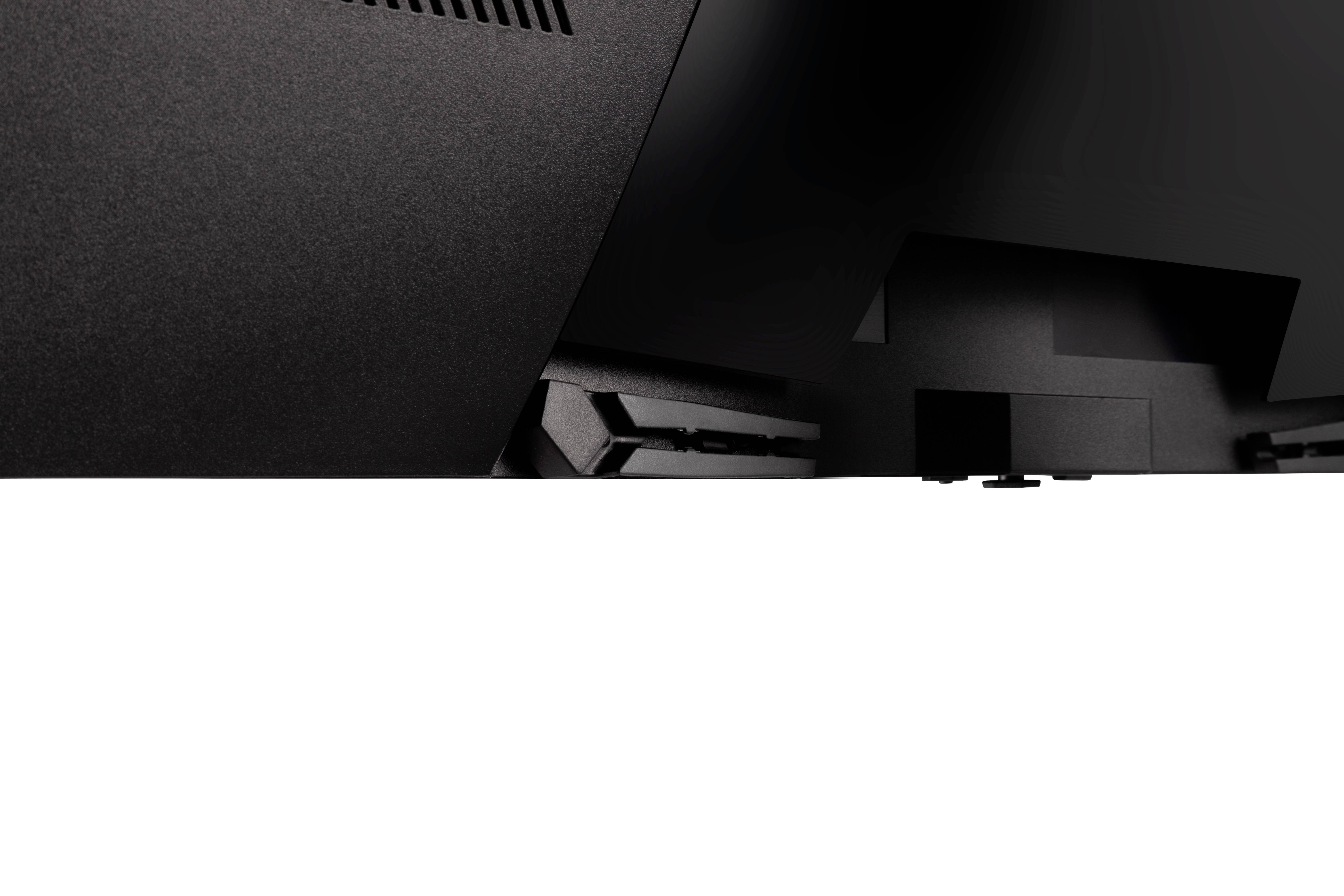 Primo piano di un dispositivo elettronico nero con fessure di ventilazione e bordi strutturati nella parte superiore dell'immagine.