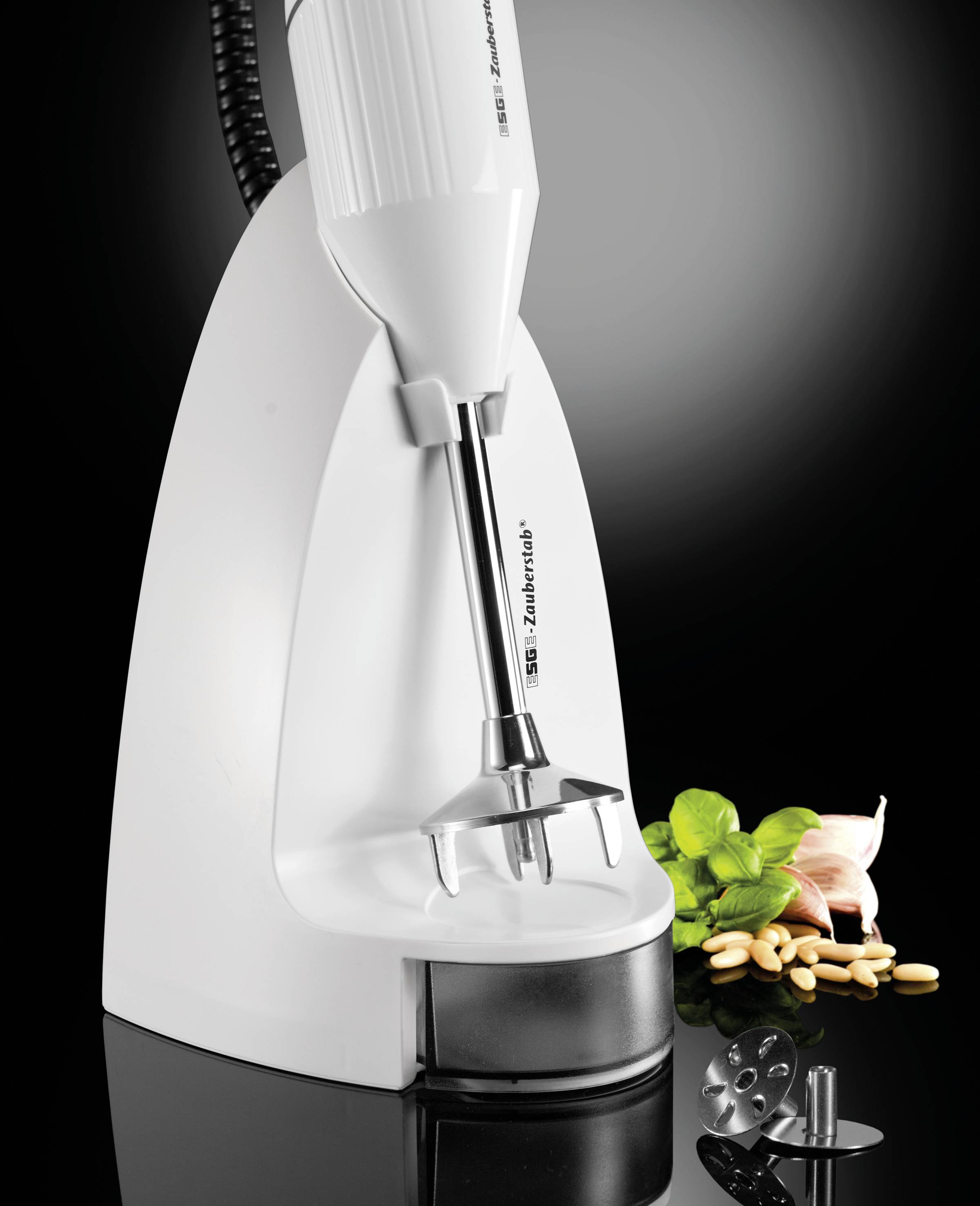 Mixer bianco da cucina su sfondo nero, con accessori per mescolare removibili. Accanto si trovano basilico, aglio e noci.