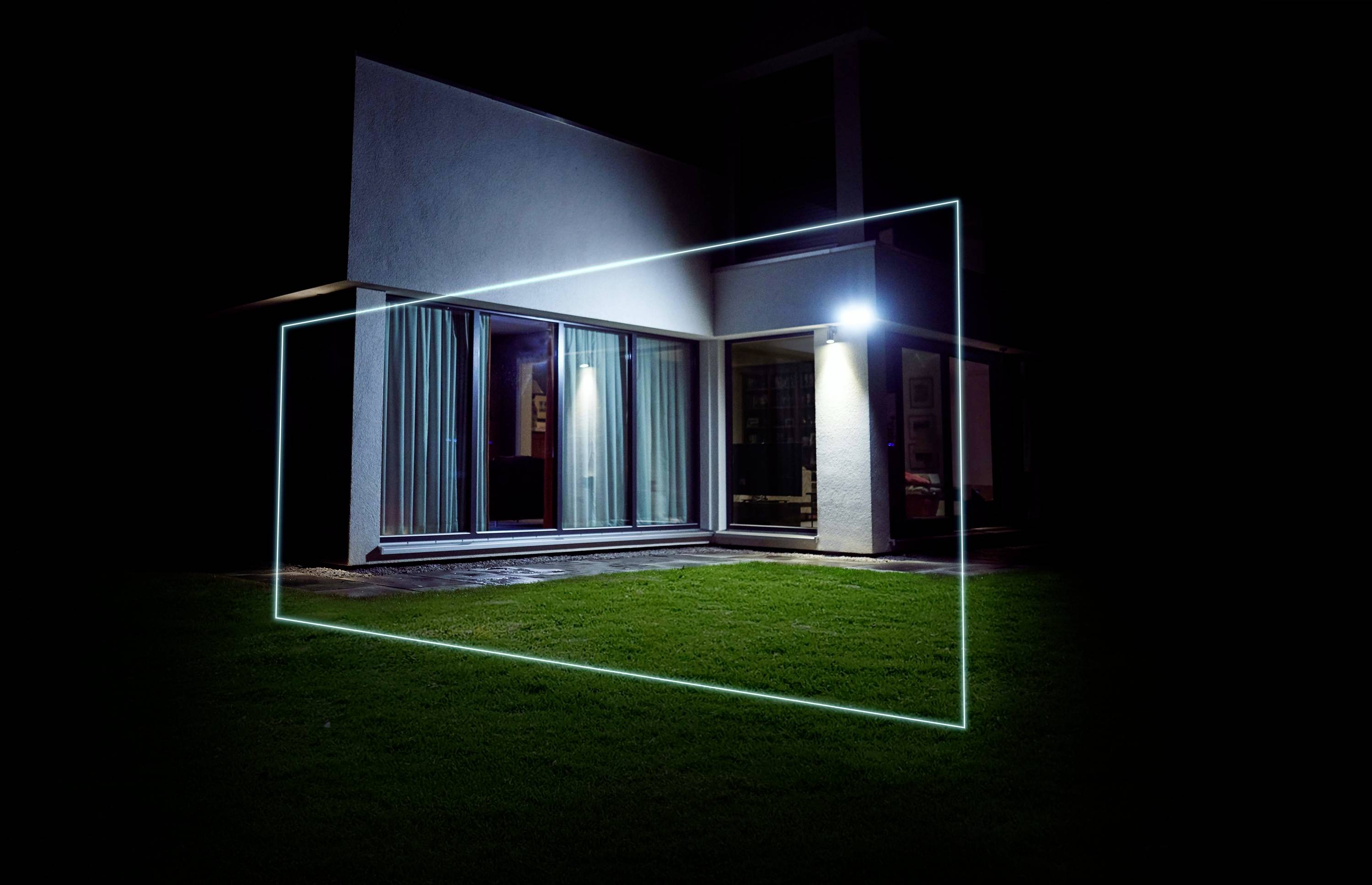 Un telaio rettangolare luminoso aleggia di notte davanti a una casa moderna su un prato, creando un effetto futuristico.