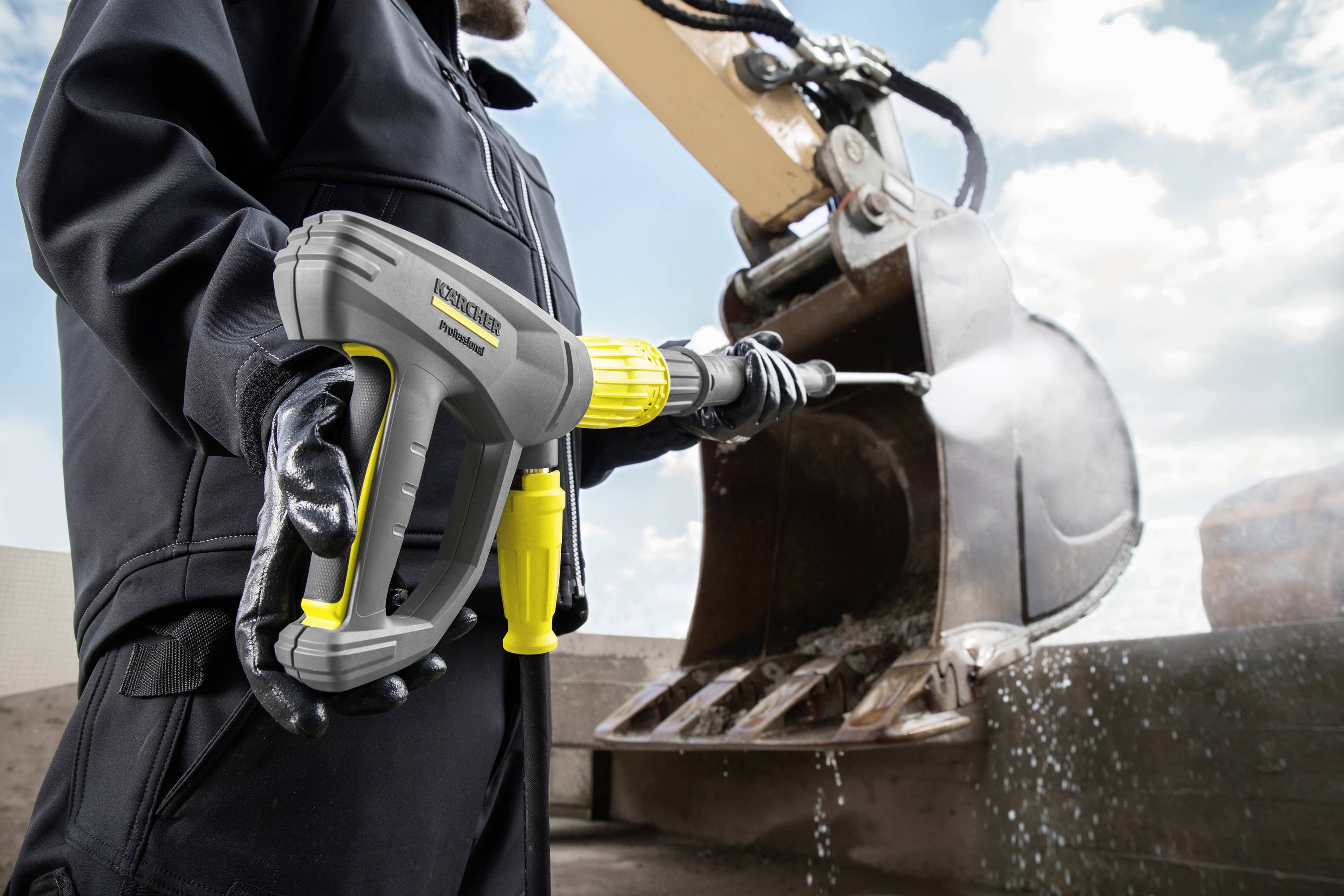 Un operaio sta pulendo con un idropulitrice la benna di un escavatore. L'acqua schizza via dalla superficie della benna.