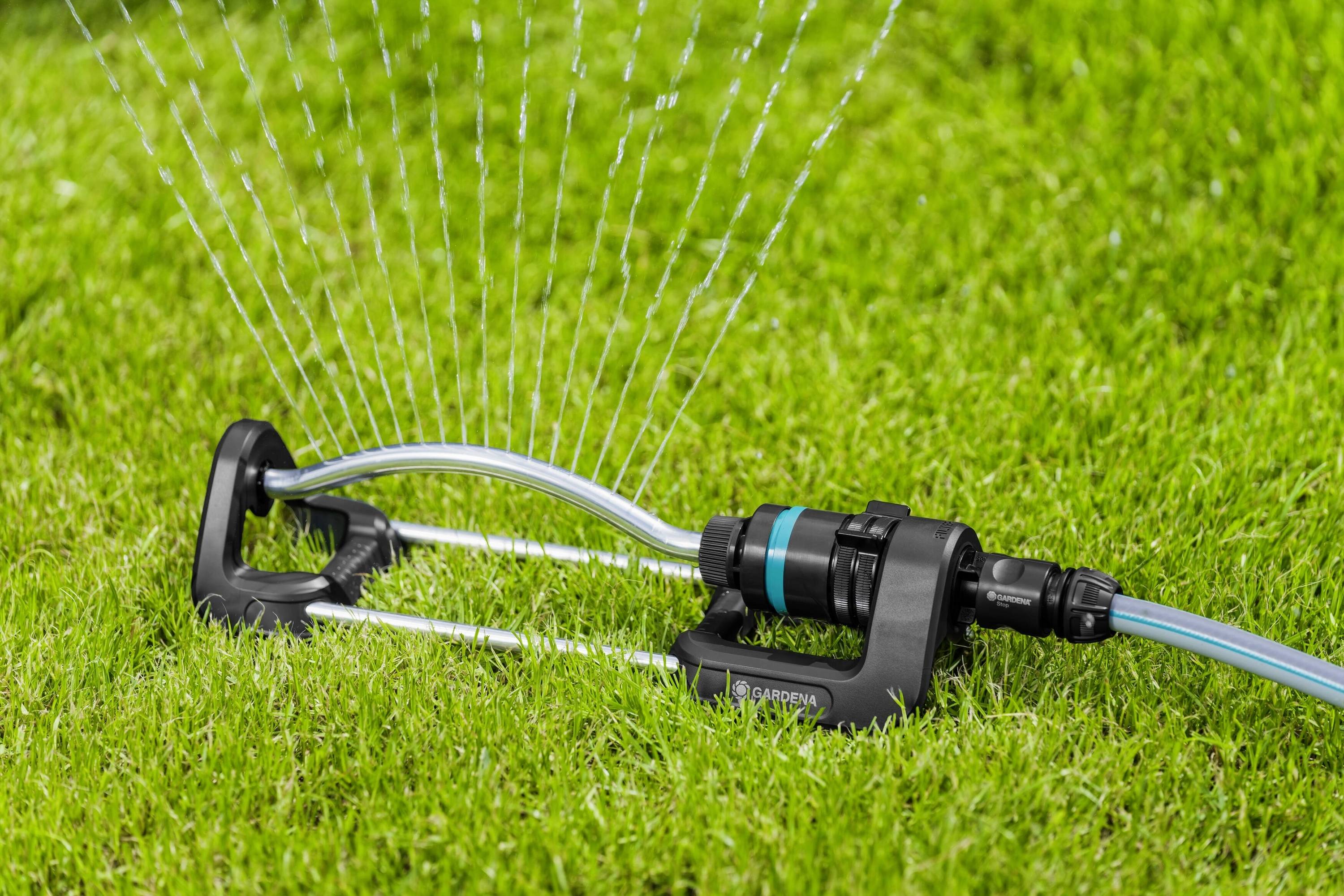 Un irrigatore spruzza acqua sull'erba verde, distribuendo sottili getti d'acqua in modo uniforme.