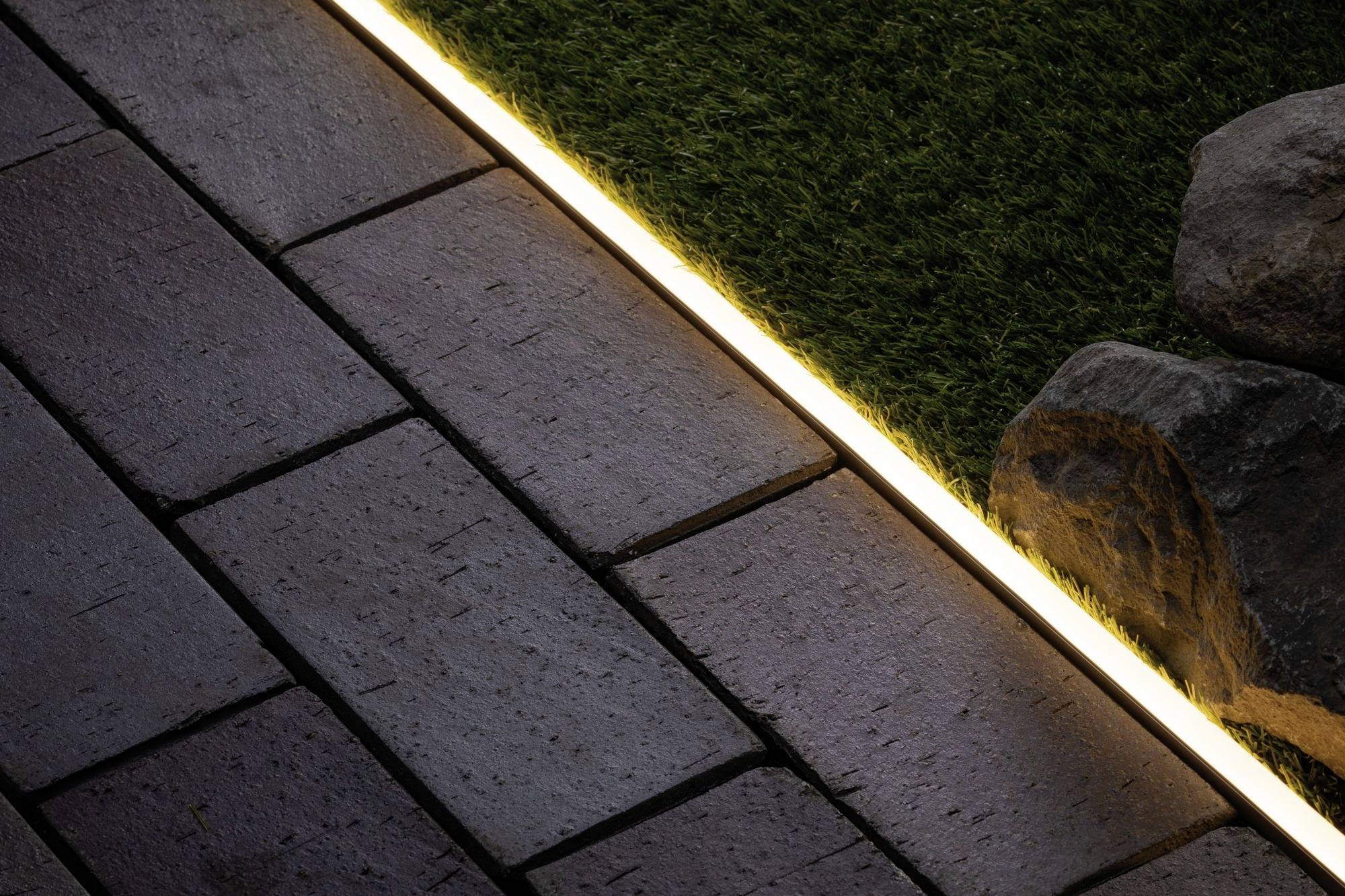 'Immagine di un sentiero illuminato con una striscia di luce tra i ciottoli e l'erba, accanto a diversi sassi.'