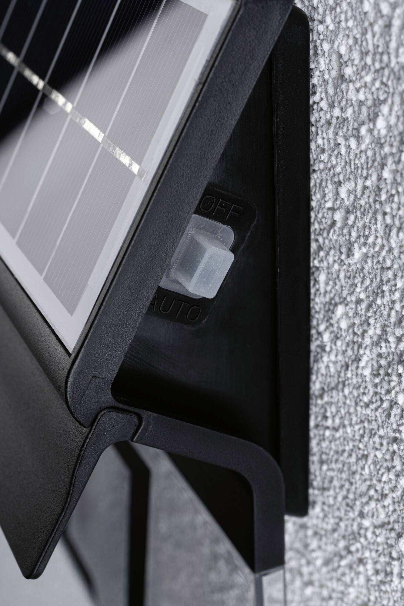 Pannello solare montato su una parete ruvida con interruttore basculante nelle posizioni 'OFF' e 'AUTO'.