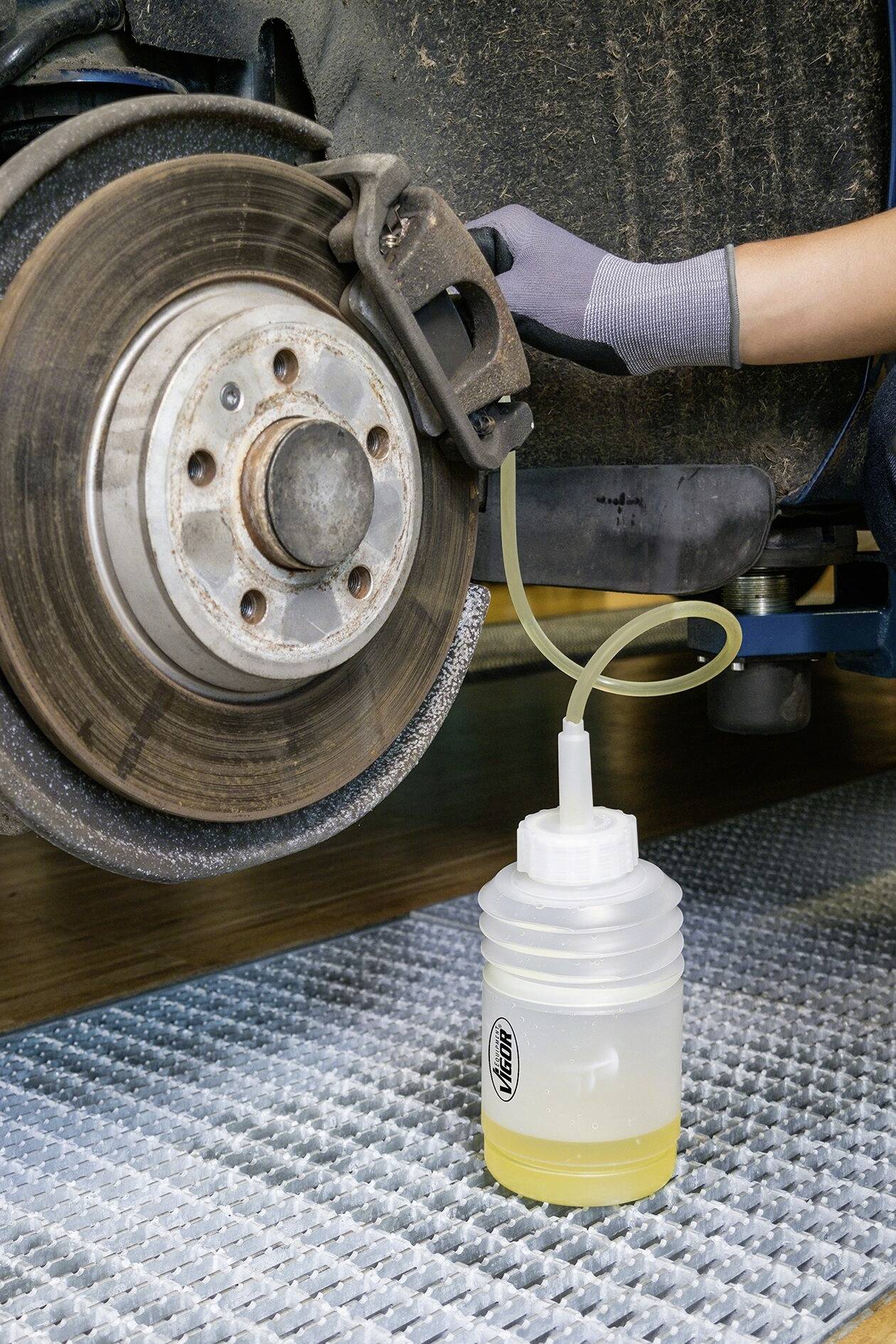 Un meccanico spurga i freni di un veicolo. Un tubo convoglia il liquido dei freni dal sistema frenante in un contenitore trasparente.