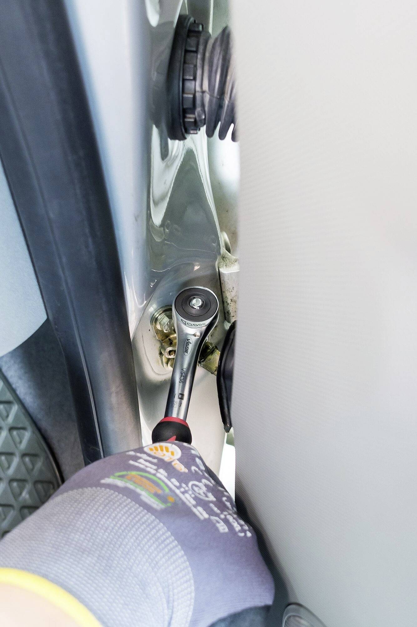 Qualcuno sta usando una chiave inglese per fissare una vite sulla cerniera di una portiera di un'automobile. Lo spazio a disposizione è molto ristretto.