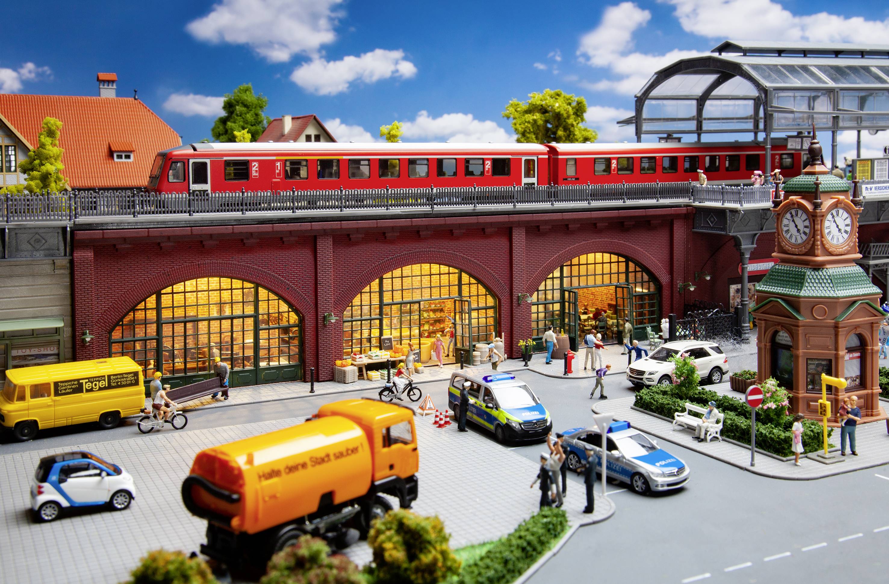 Un modello di città con un ponte levatoio, un treno rosso, edifici e veicoli sulla strada. Persone si muovono nella vita urbana frenetica.