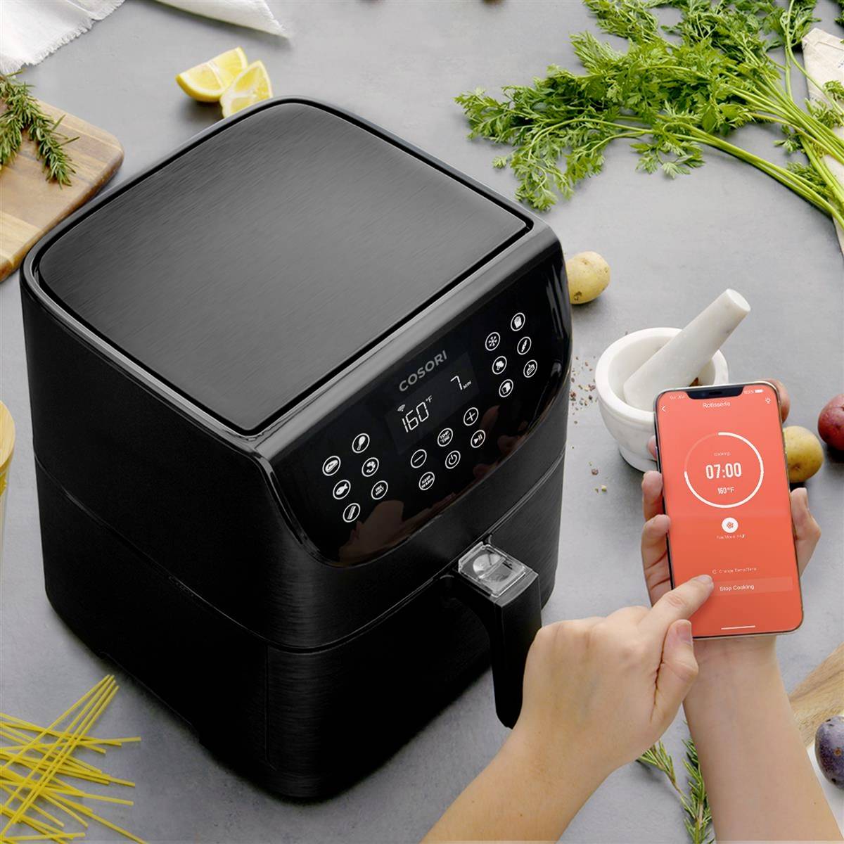 Una persona imposta un timer su uno smartphone mentre si trova accanto a una friggitrice ad aria per cucinare.